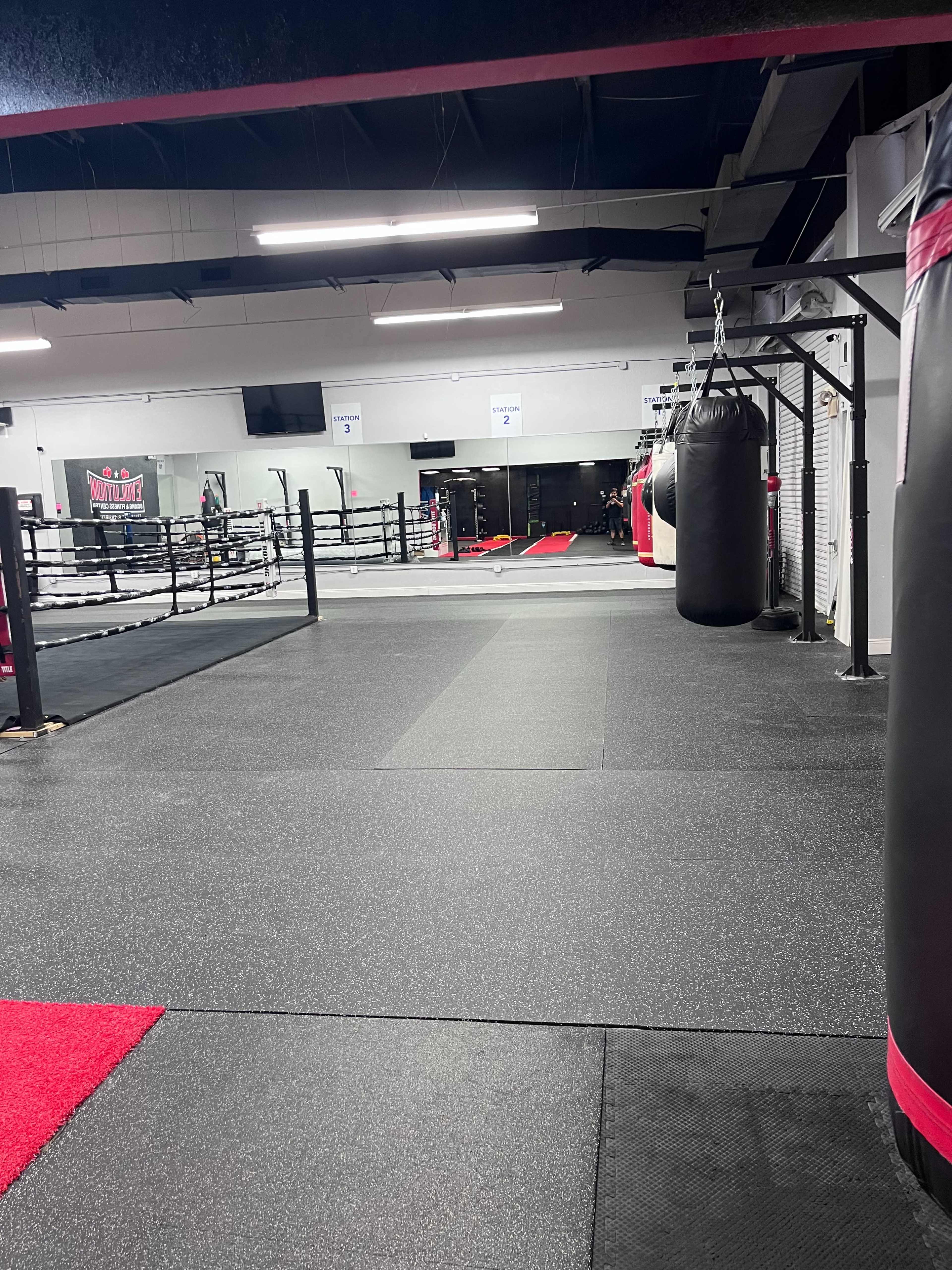 An empty boxing gym featuring a ring, punching bags, and rubber flooring.