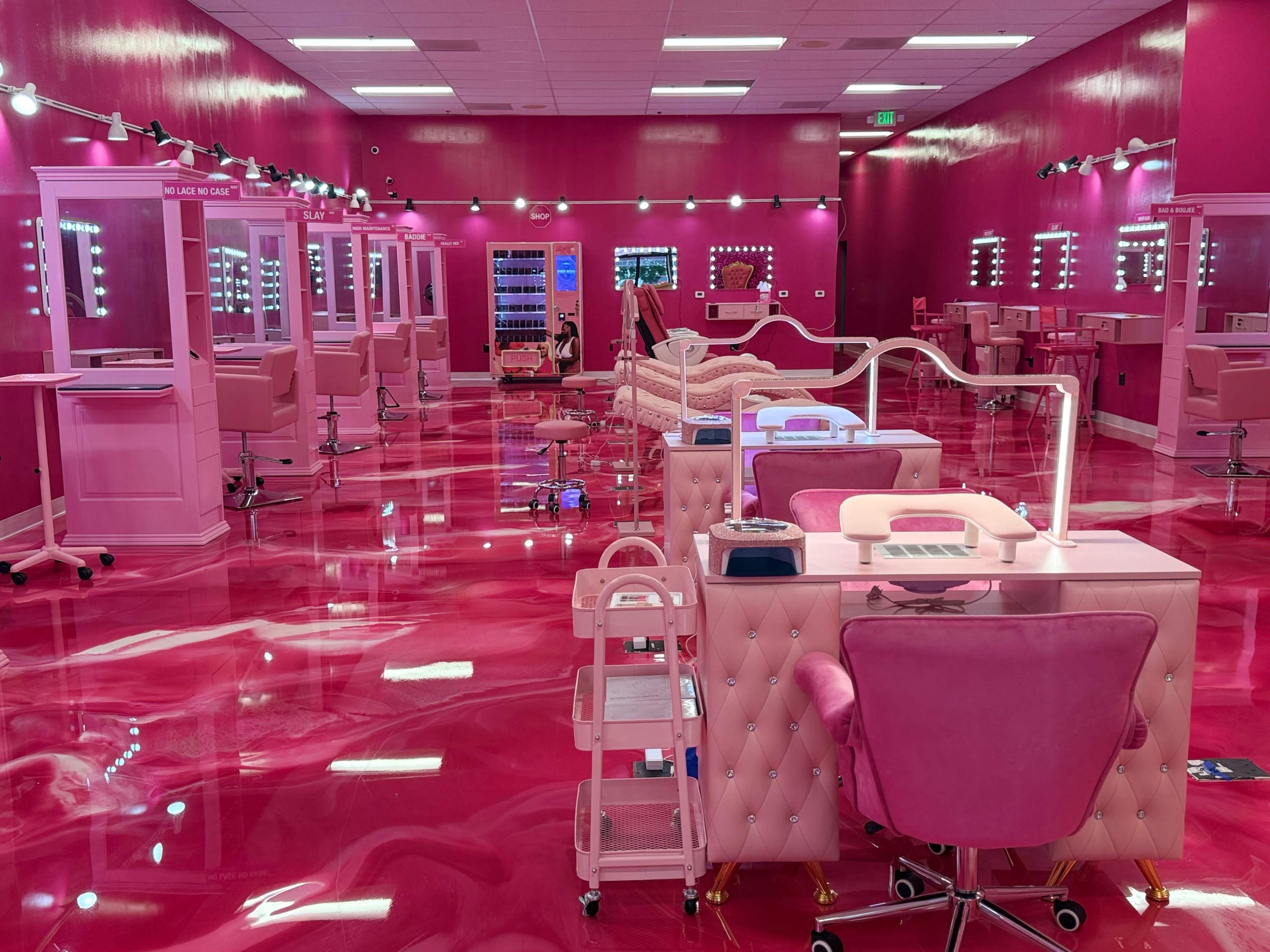 The image shows a vibrant pink nail salon with mirrored stations, pedicure chairs, and bright lighting.