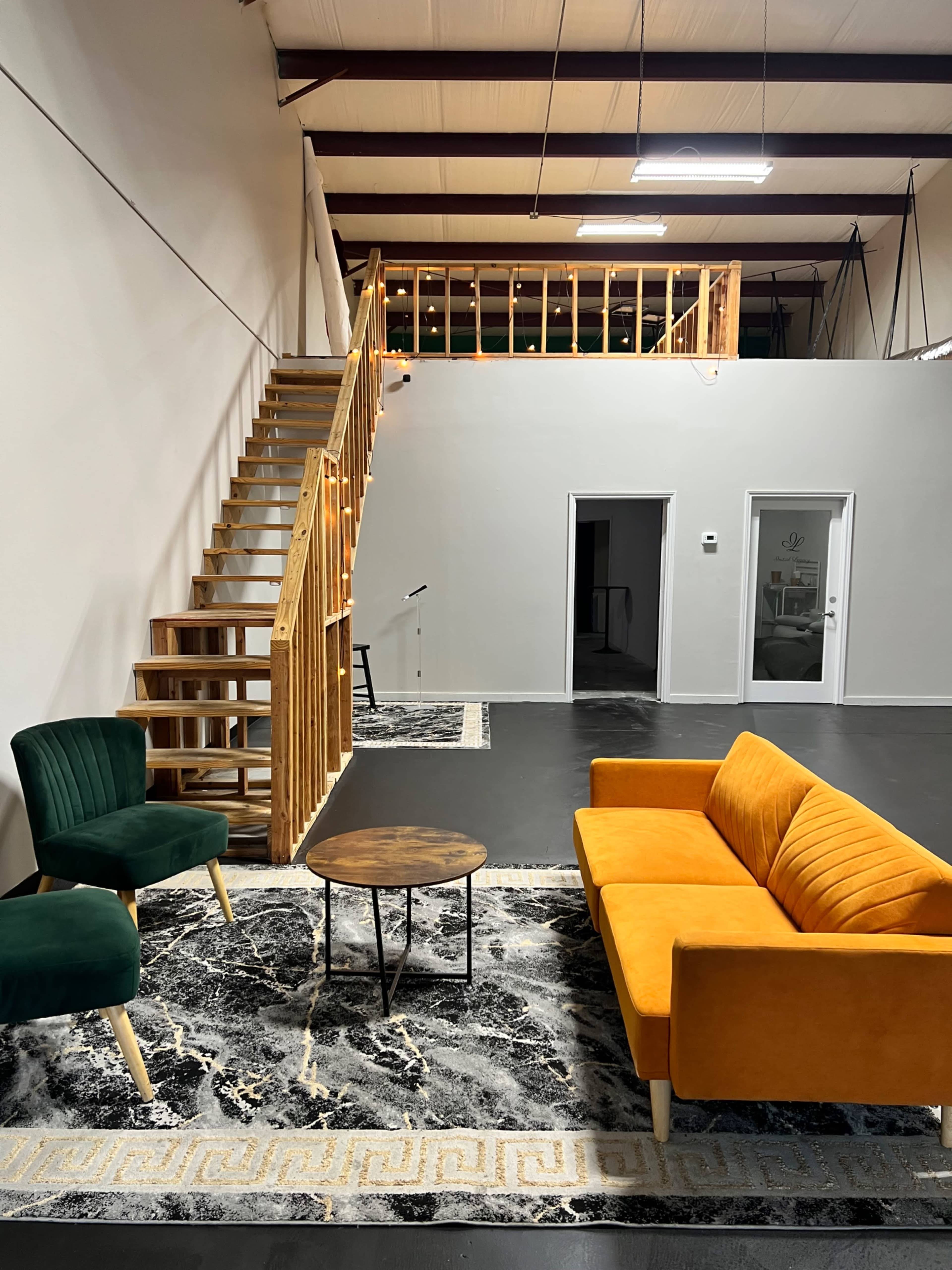 The image shows a spacious interior with a two-tone orange and green seating area, a round coffee table, a patterned rug, and a staircase leading to an upper level.