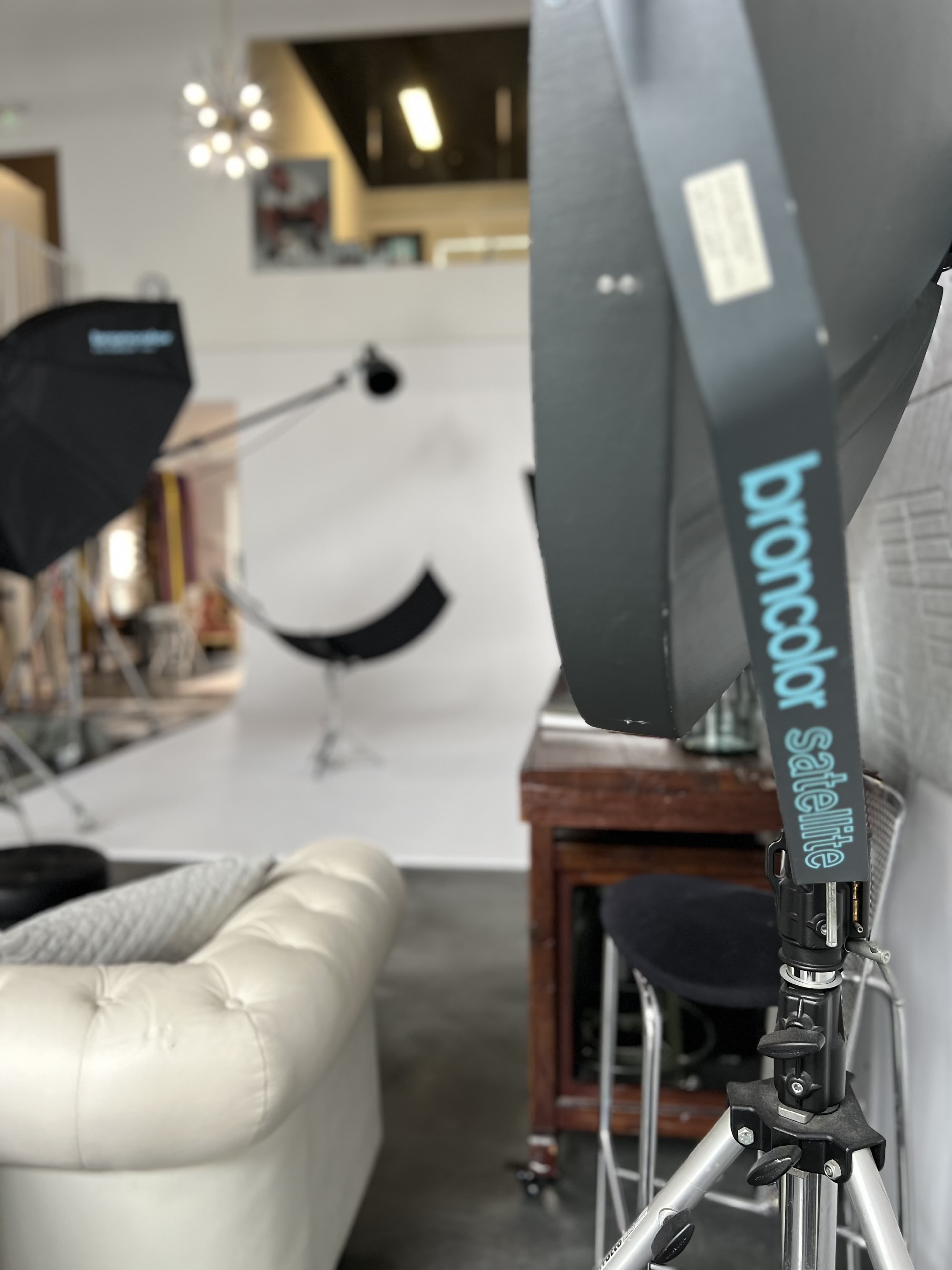A photography studio with softbox lighting, a white backdrop, and a vintage wooden table alongside modern furniture.