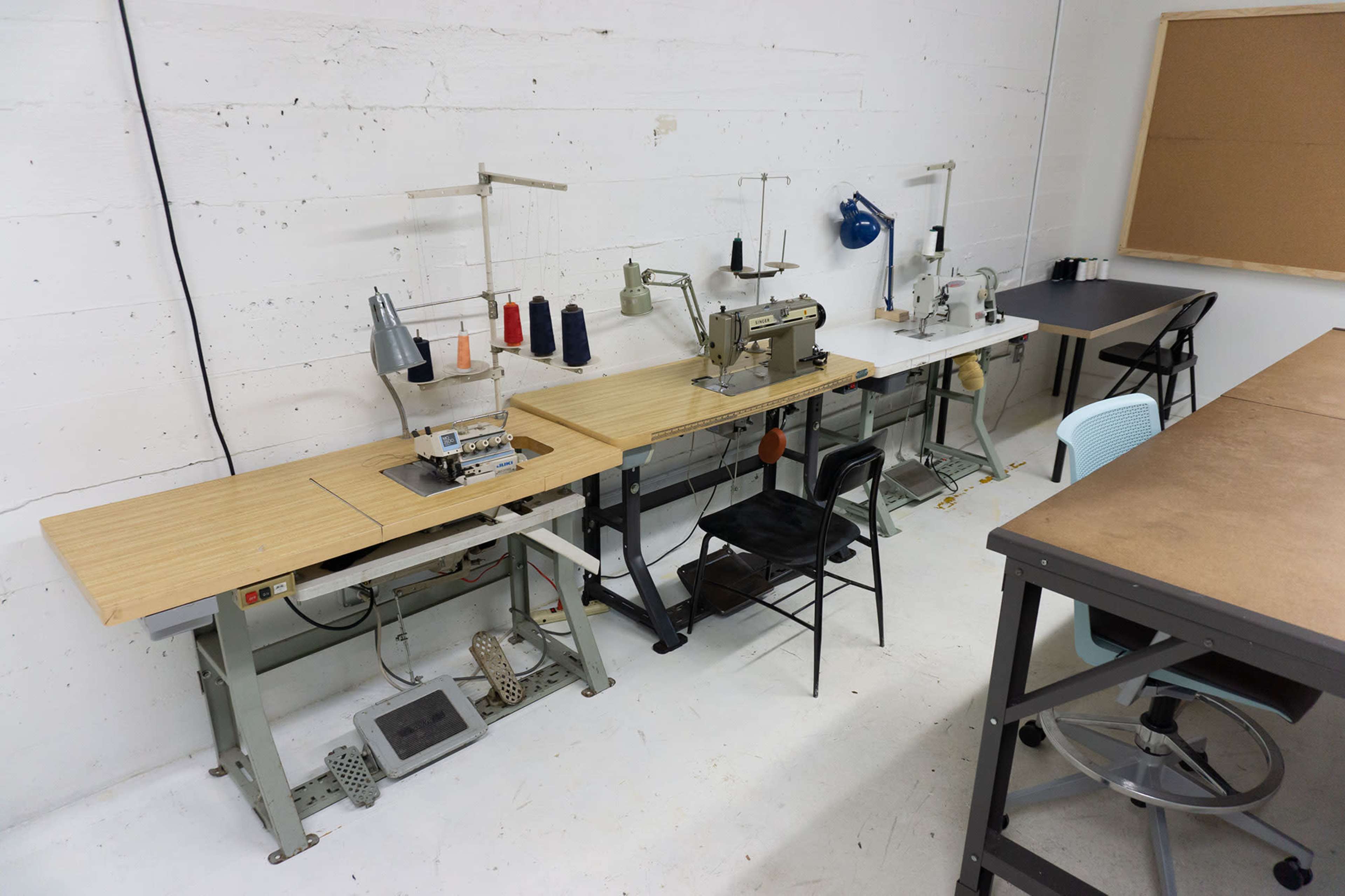 A row of sewing machines arranged on wooden tables in a well-lit room.