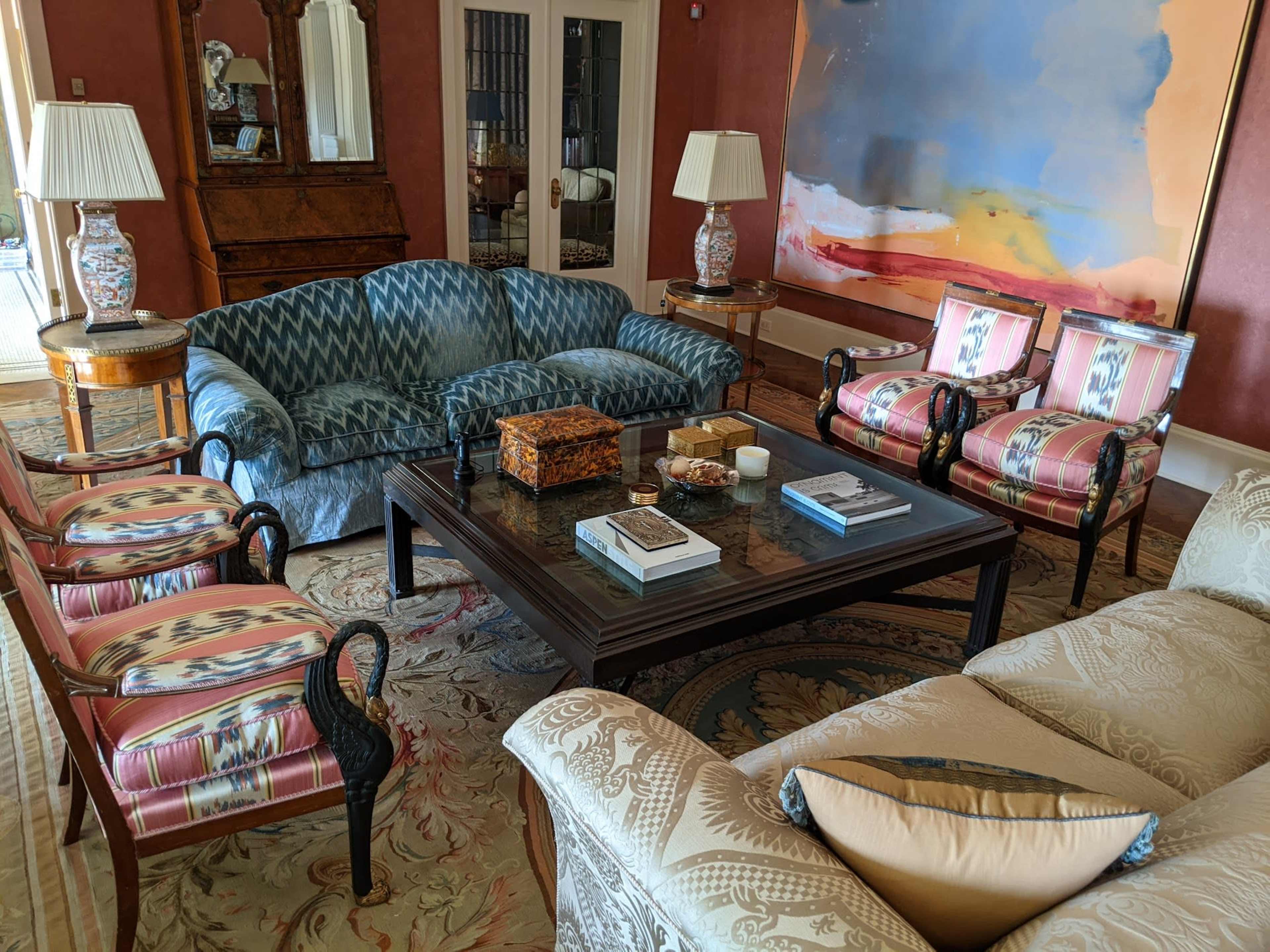 A spacious living room features a mix of seating, including patterned sofas and armchairs, arranged around a central coffee table with decorative items.
