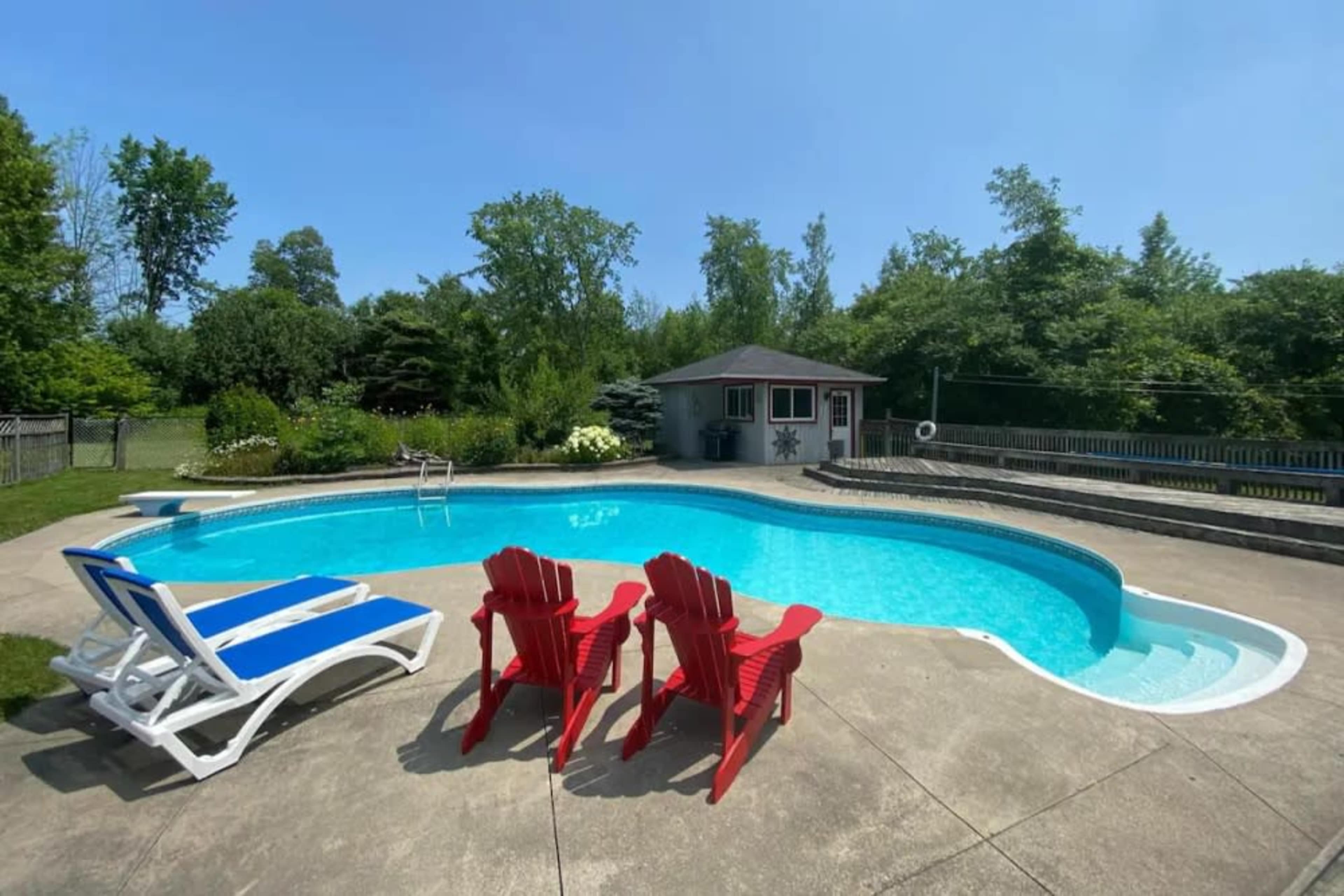 A spacious in-ground pool surrounded by red lounge chairs and a shaded cabana in a landscaped backyard.