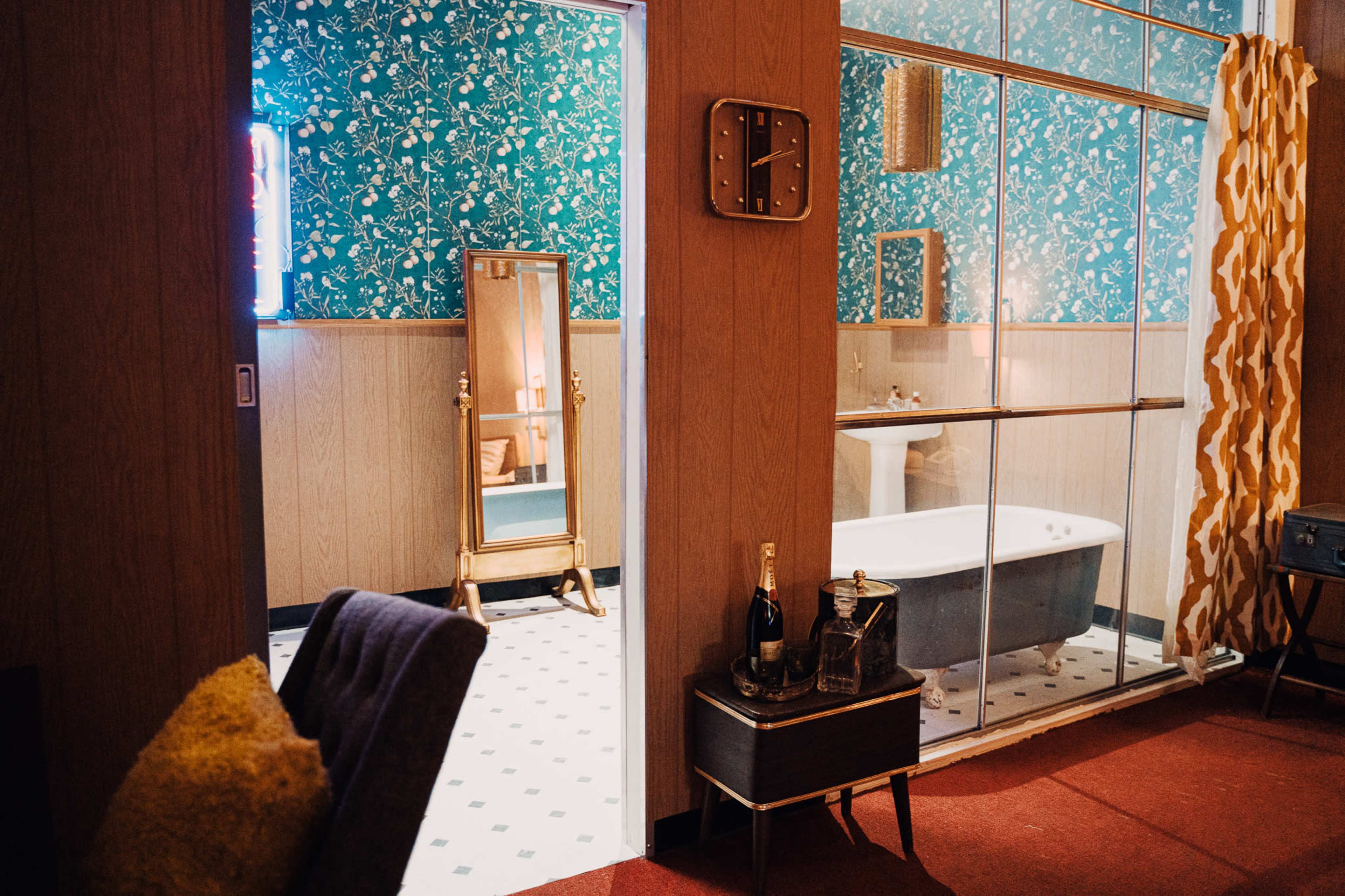 A bathroom features a freestanding bathtub enclosed by glass, with a mirror and floral wallpaper visible in a stylish interior setting.