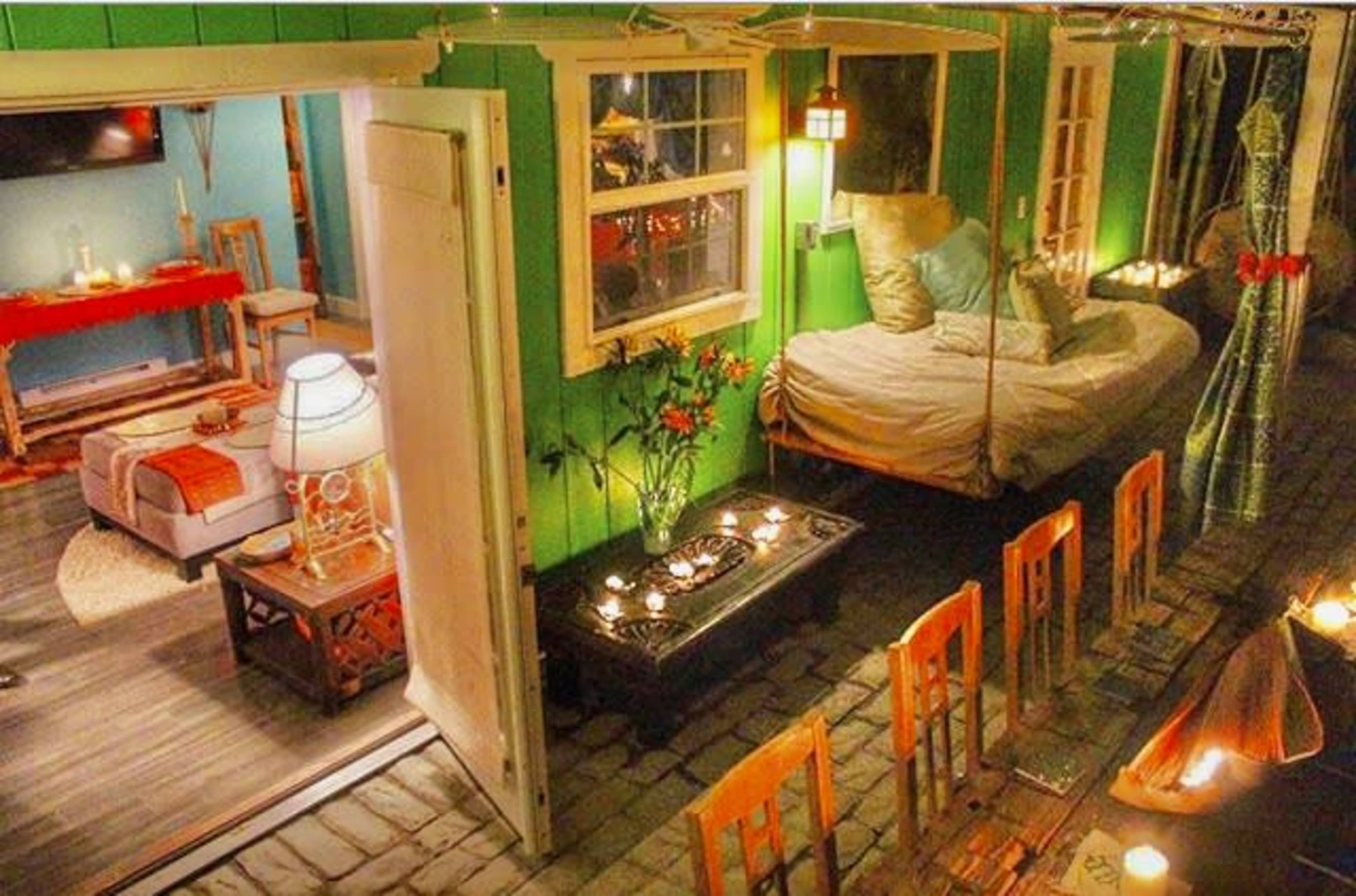 A cozy interior of a brightly colored room featuring a bed, a seating area, and a dining table adorned with candles.