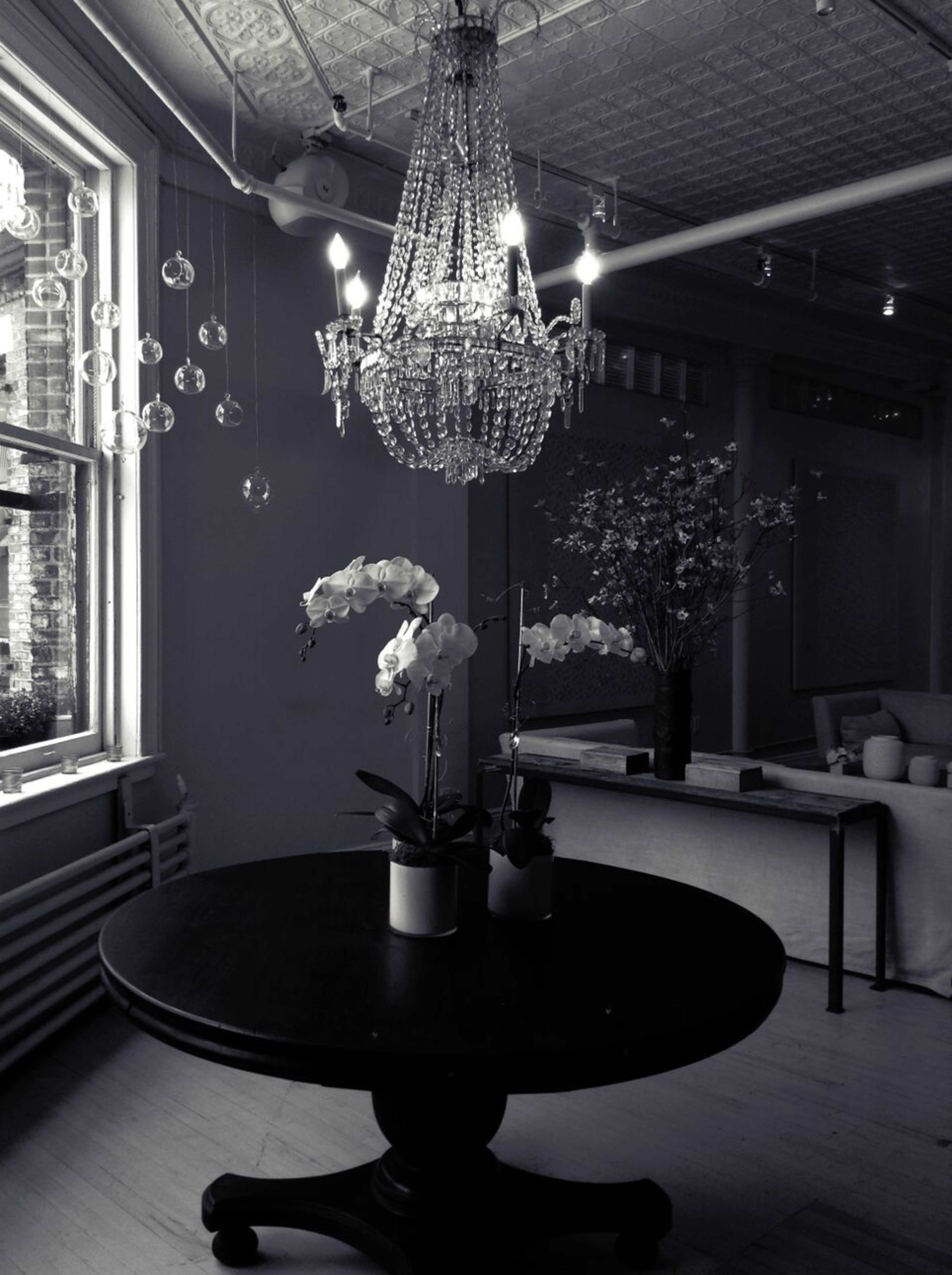A crystal chandelier hangs above a dark wooden table adorned with two potted orchids in a well-lit room.