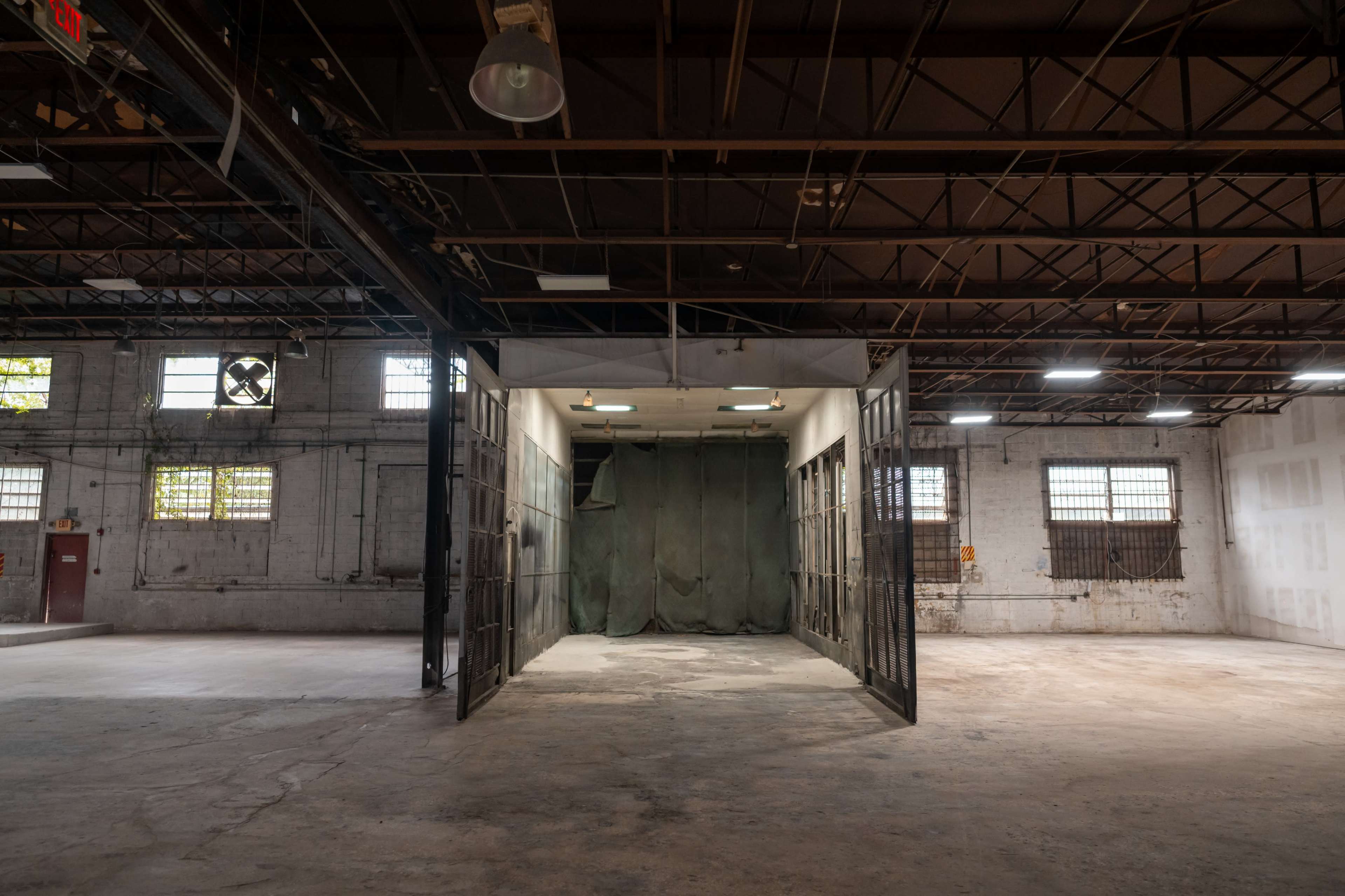 The image shows a spacious industrial room with an open doorway leading to another area, featuring concrete floors and exposed metal beams overhead.