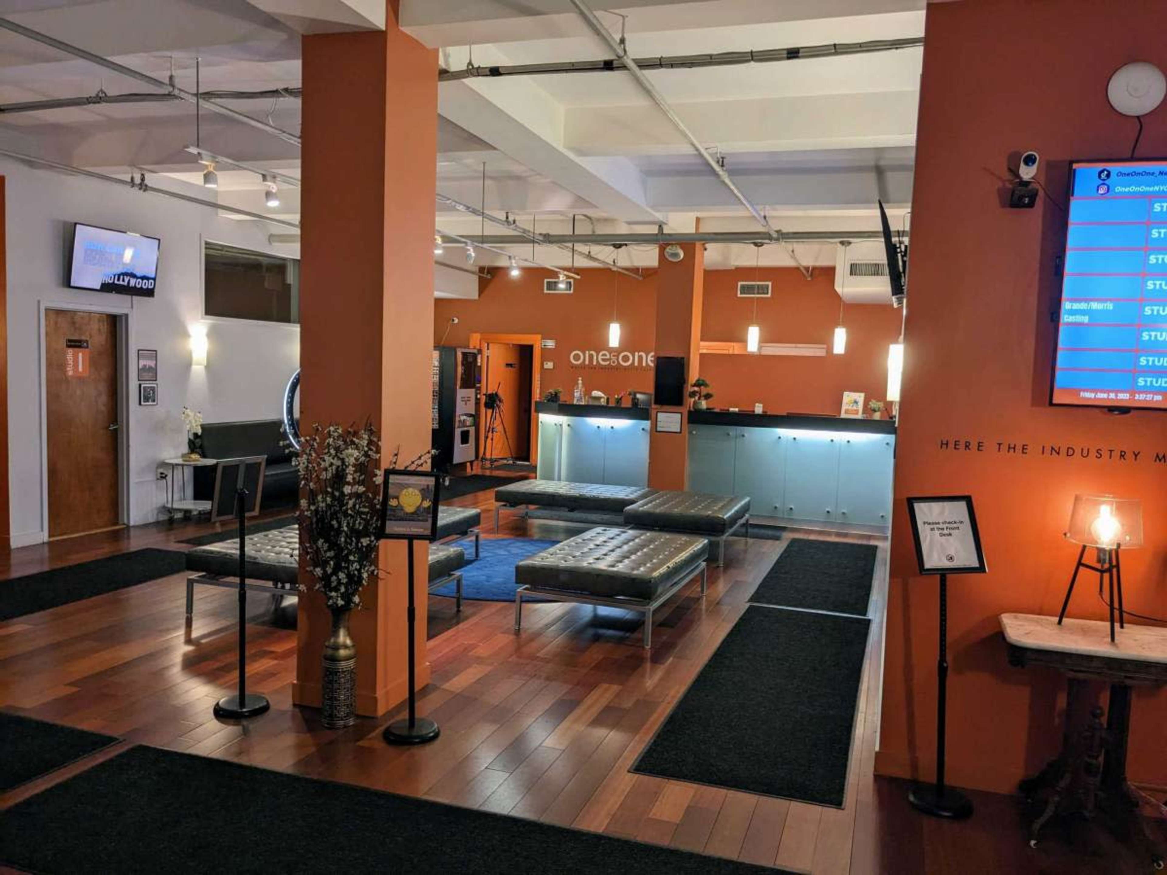 The image shows a modern reception area with a sleek front desk, benches for seating, and an orange wall displaying the "ones:one" logo.