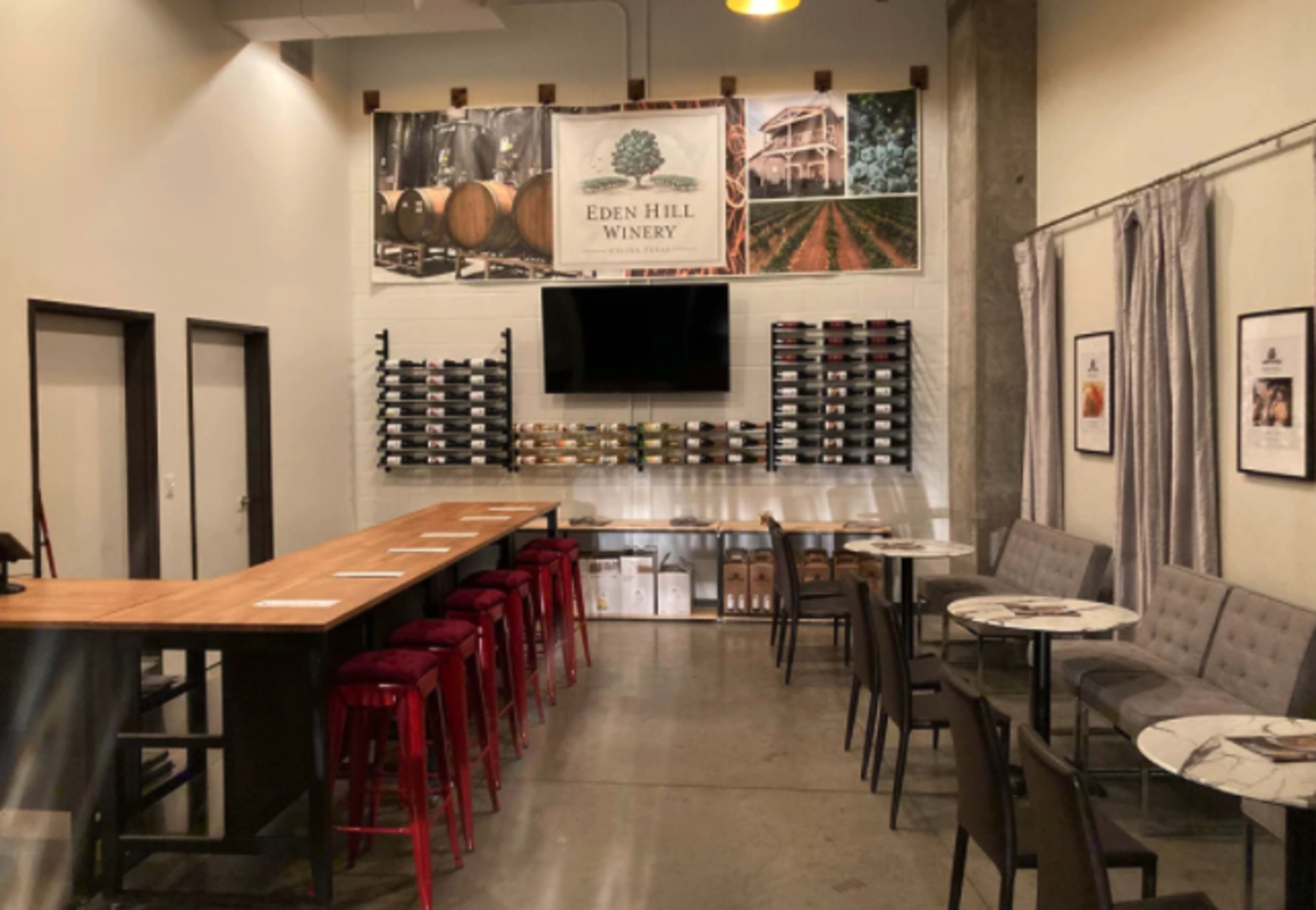 A modern wine tasting room featuring a large wooden bar, rows of wine bottles on shelves, and seating areas with tables and chairs.