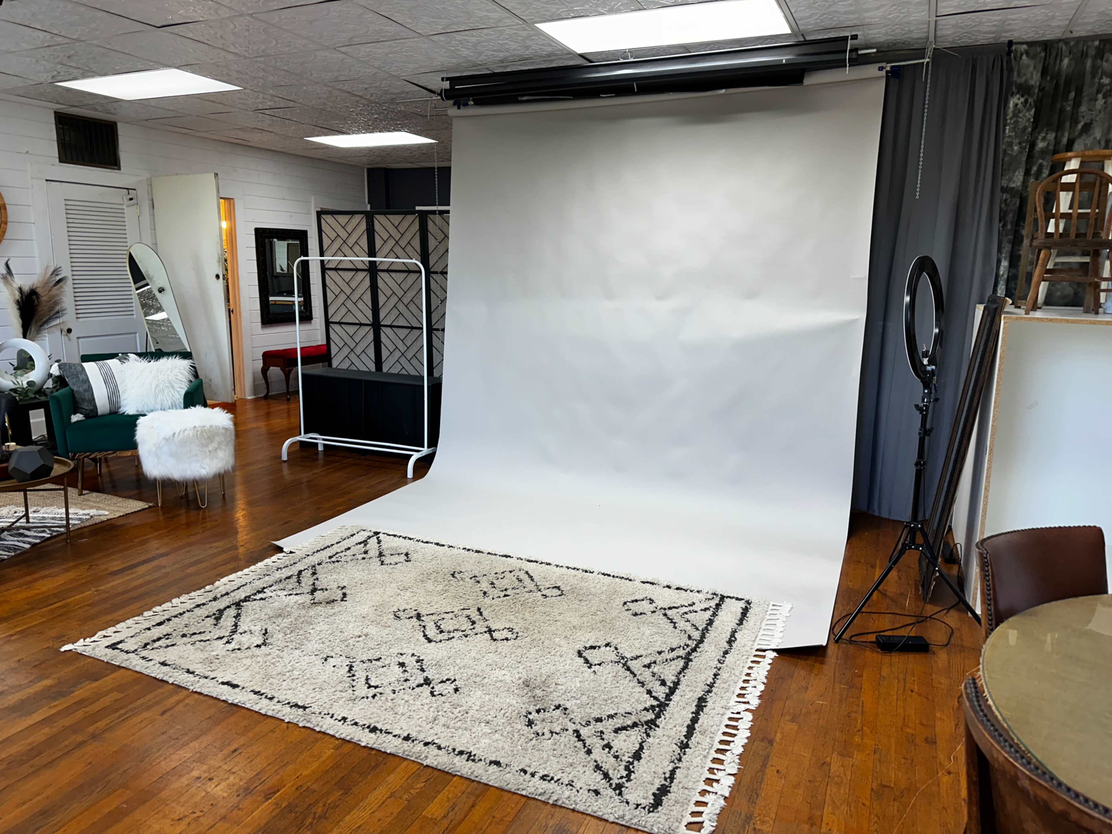A photography studio featuring a plain backdrop, a decorative rug, and various furniture pieces arranged around the space.