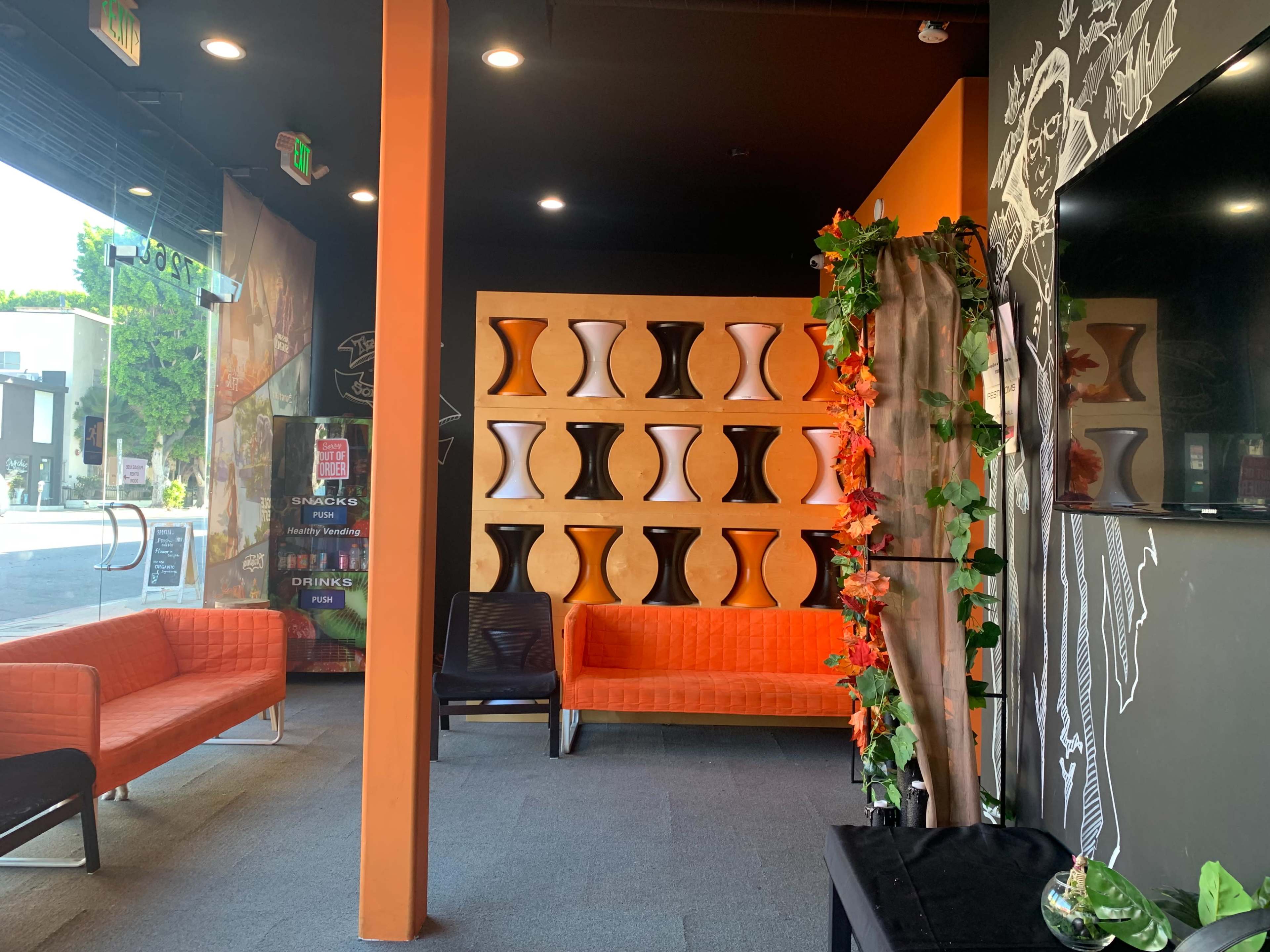 A lounge area with orange couches, a decorative wall featuring vases, and green vines.
