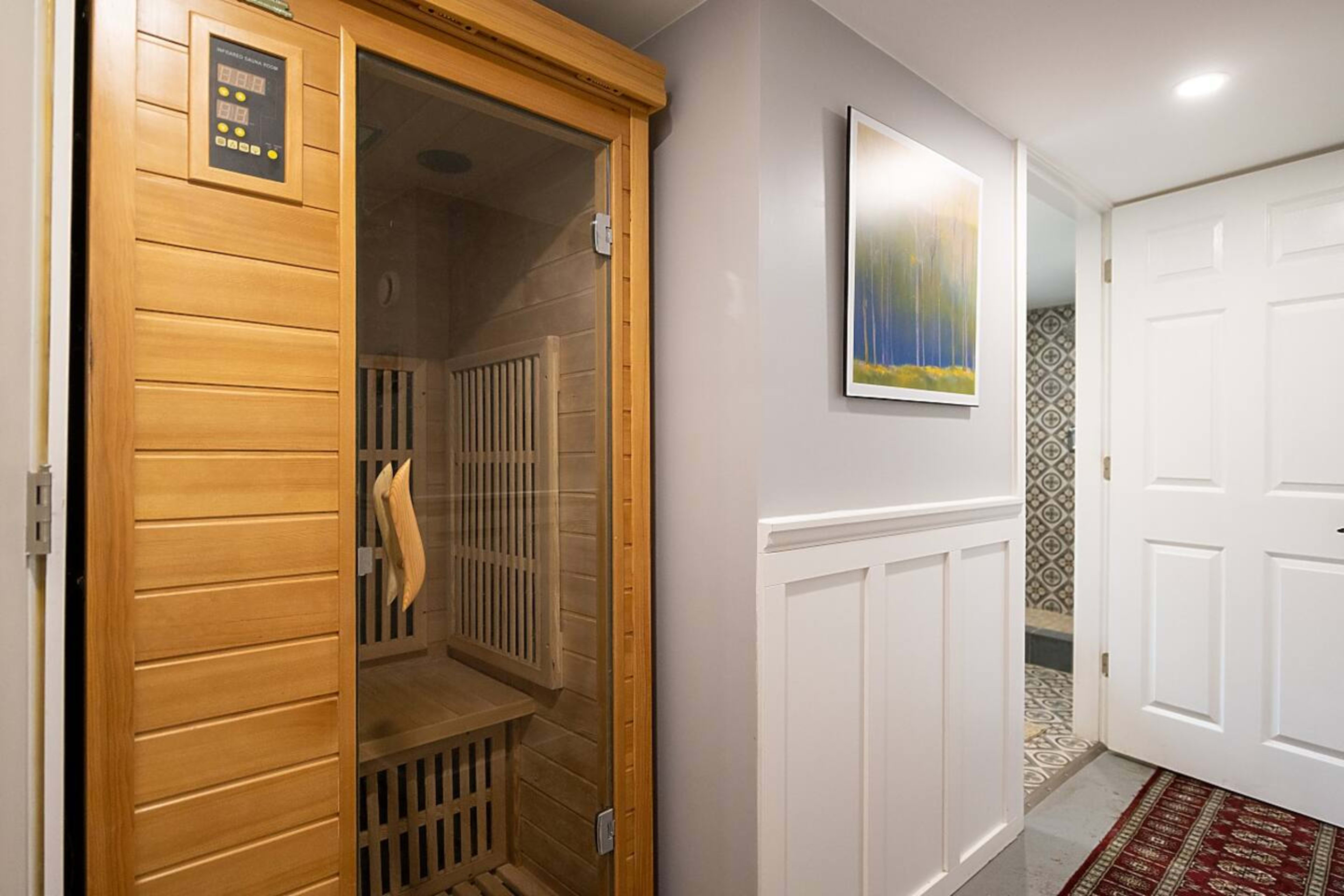 A wooden sauna positioned in a hallway, adjacent to a decorative wall and a doorway leading to another room.