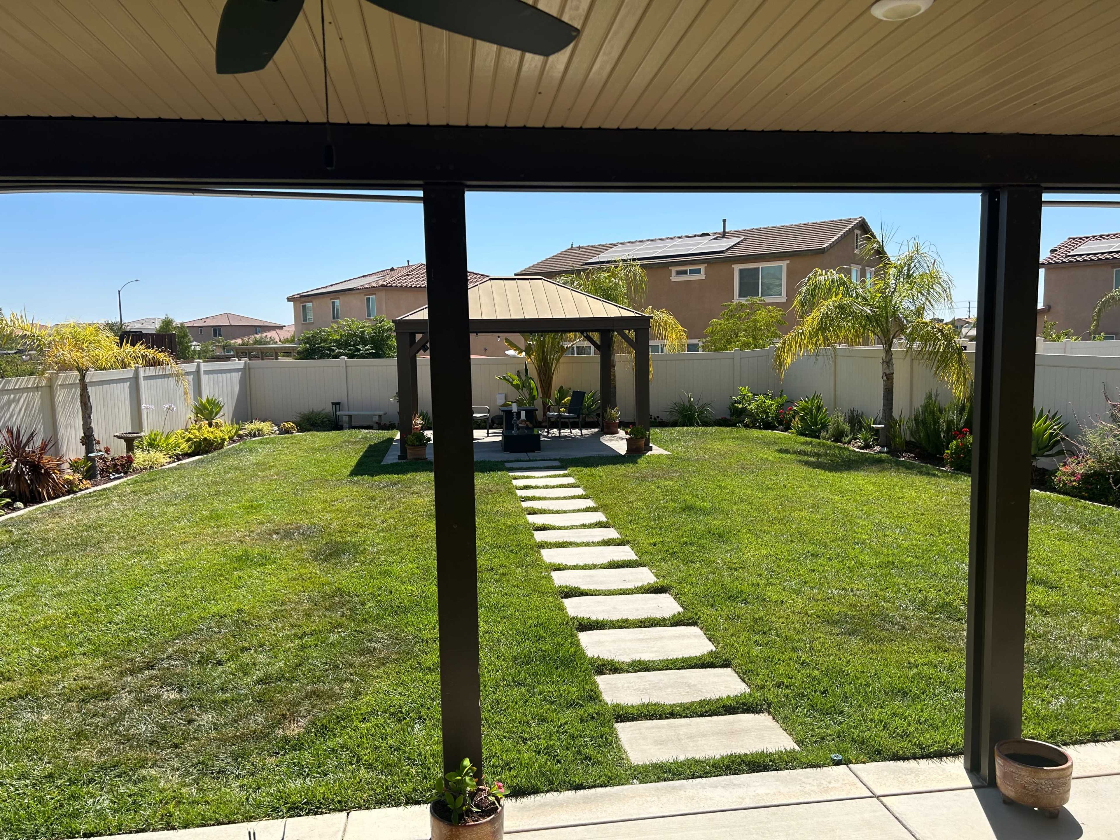 A landscaped backyard features a gazebo surrounded by neatly trimmed grass and stone pathways, with homes visible in the background.