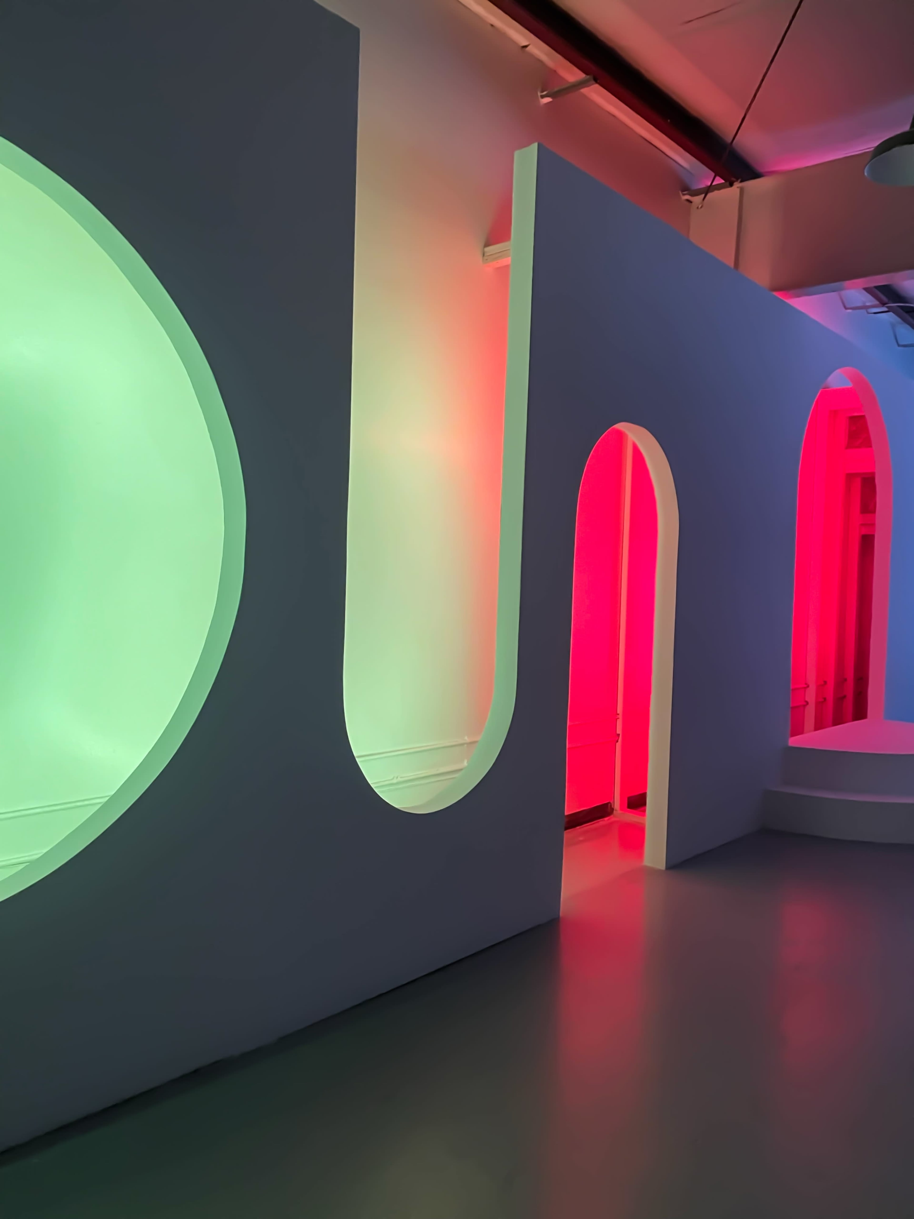 The image shows a modern interior with curved walls illuminated in green and red light, featuring several arched doorways.