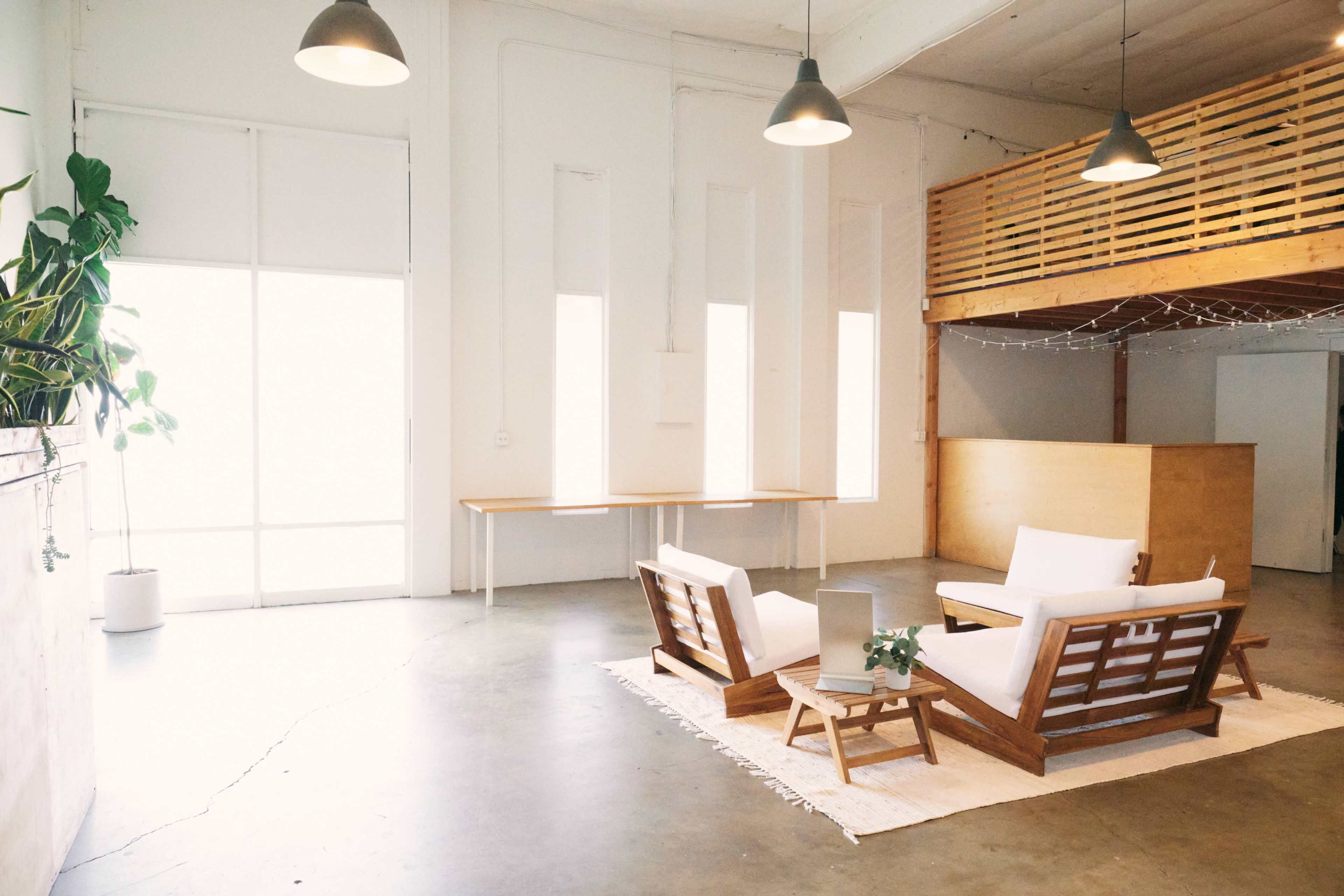 A spacious, modern interior with a seating area featuring wooden furniture, a small table, and a loft area in the background.