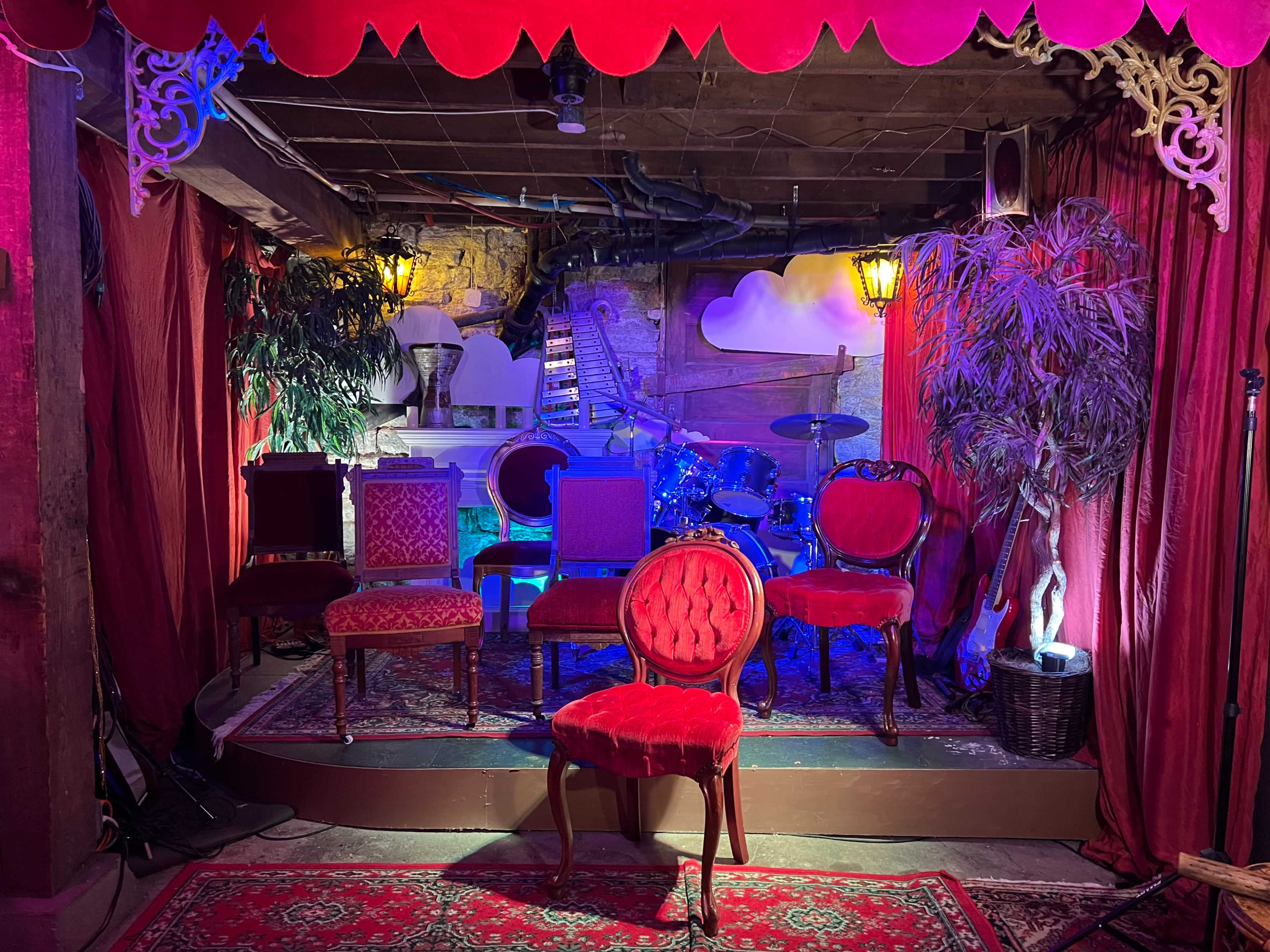 The scene features a small stage adorned with various chairs, musical instruments in the background, and decorative elements such as plants and lamps.