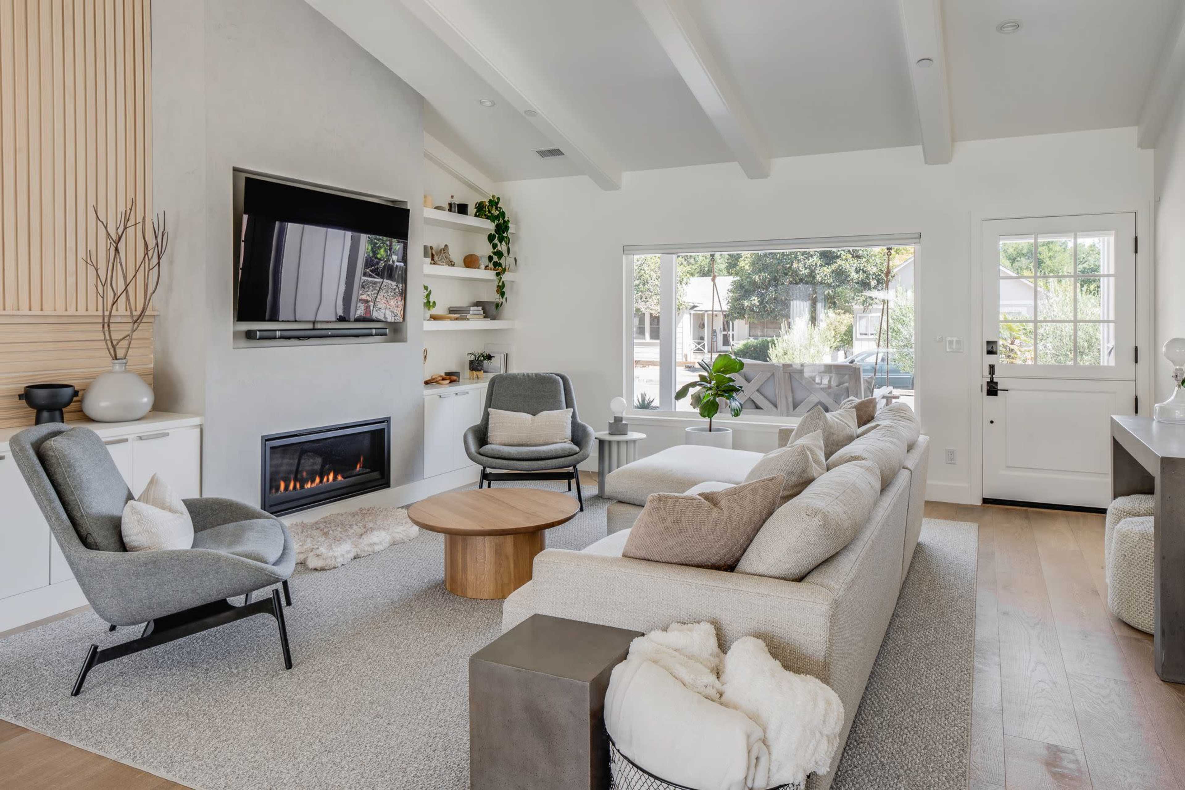 The living room features a modern design with a gray sofa, a wooden coffee table, and a fireplace beneath a mounted television.