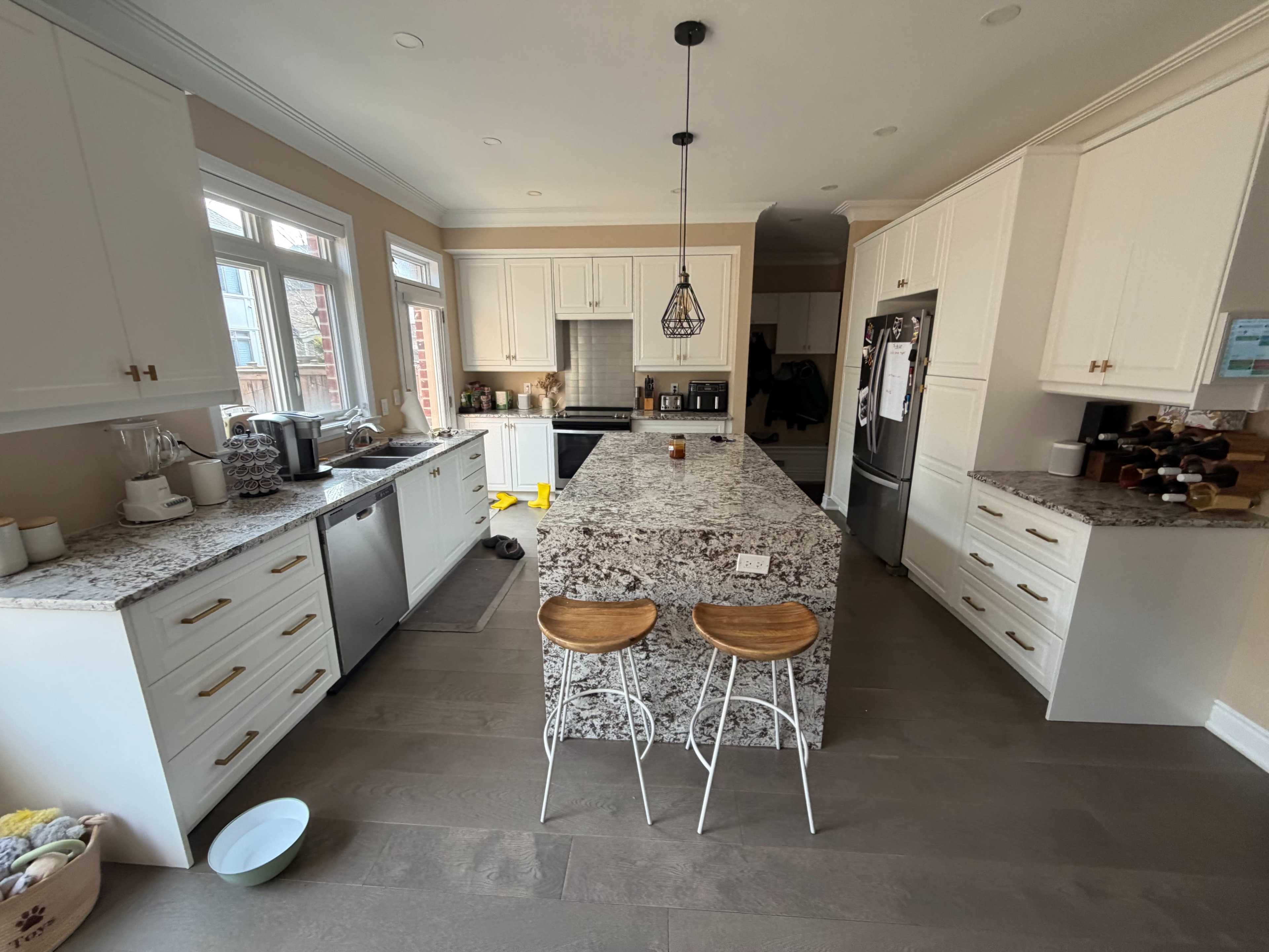 A modern kitchen features white cabinetry, granite countertops, and a central island with two bar stools.
