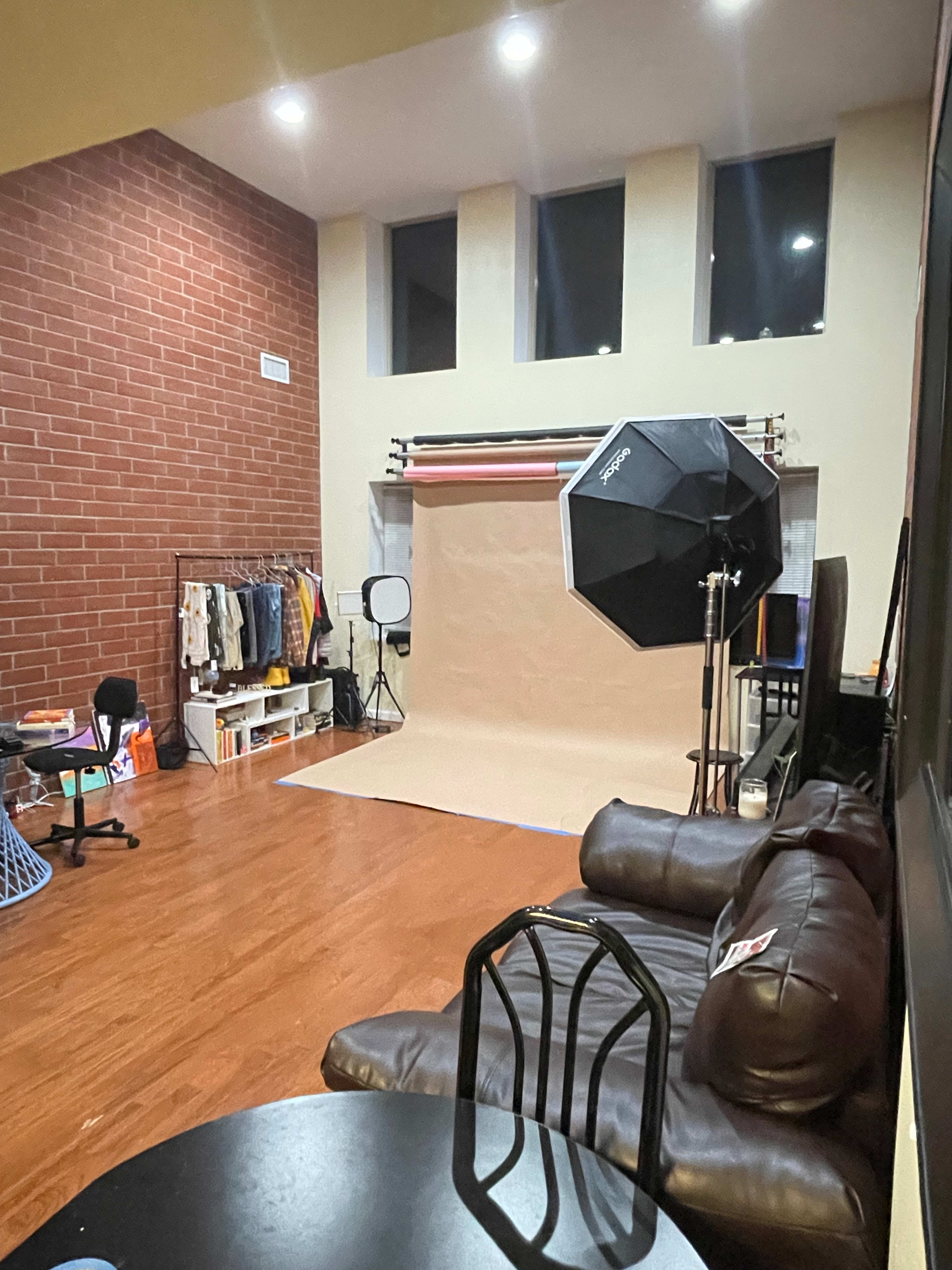 A photography studio with a backdrop setup, lighting equipment, and a seating area featuring a couch and a small table.