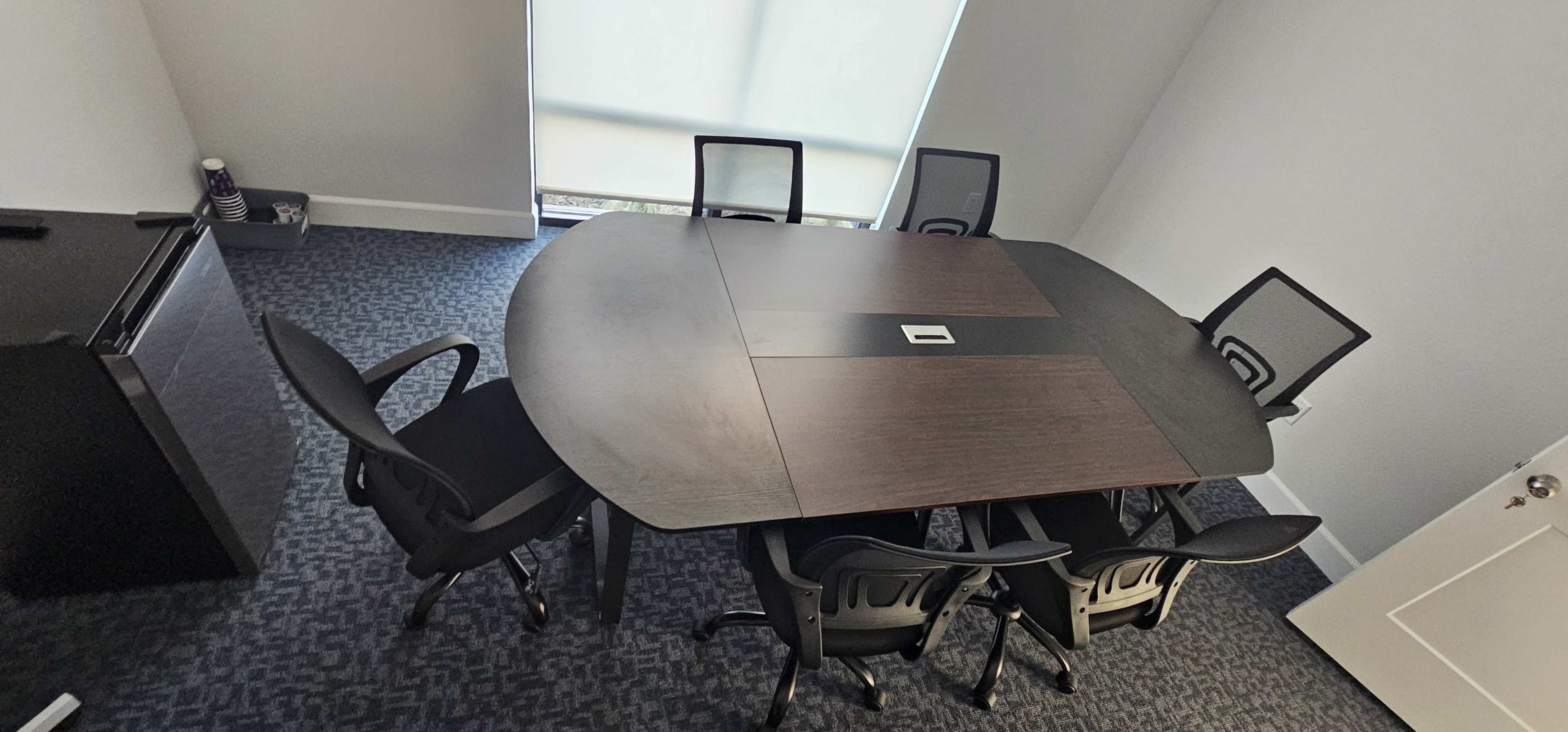 A large oval conference table is surrounded by six black chairs in a well-lit meeting room.