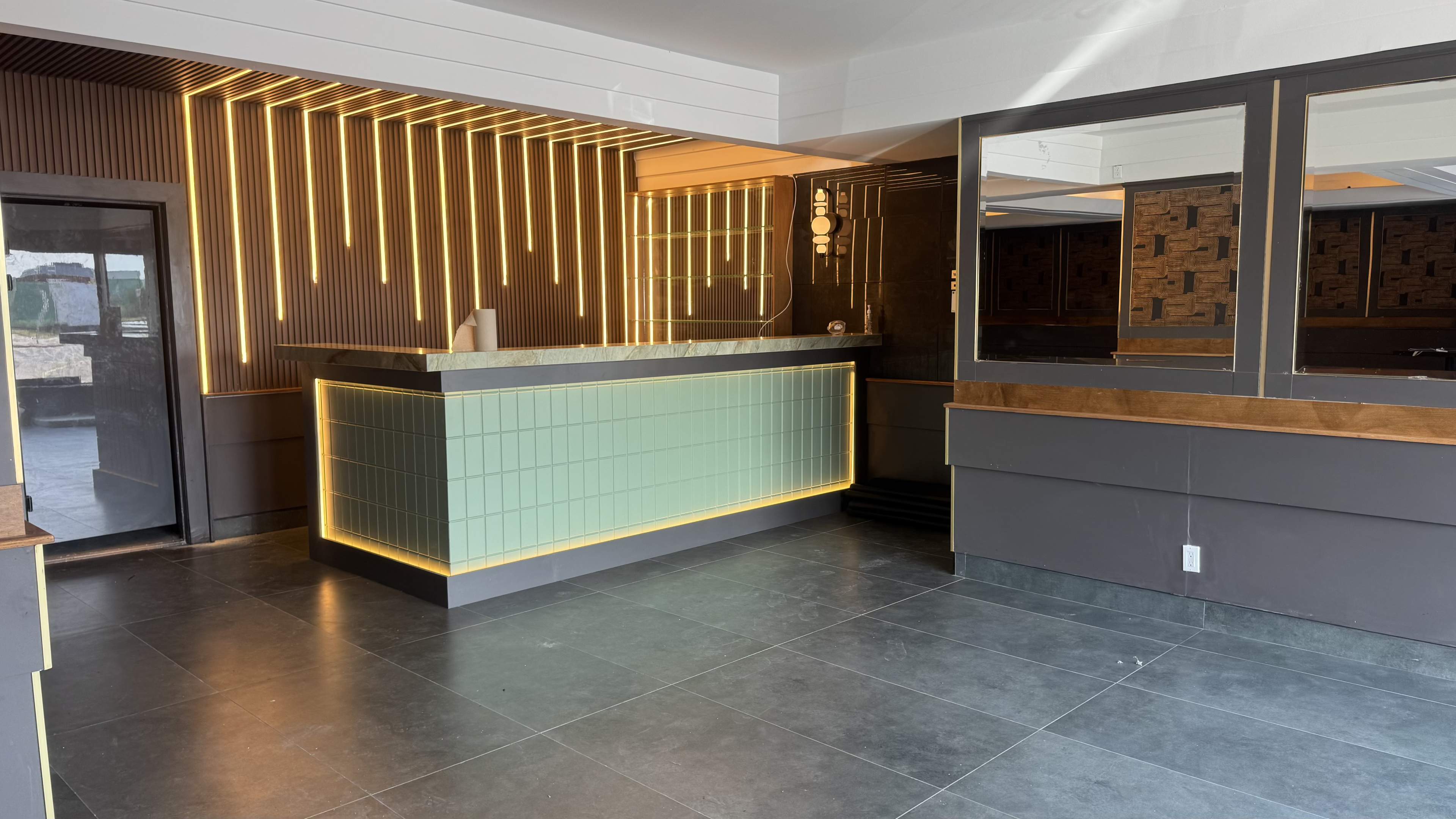 The image shows a modern reception area with a green and gold accent counter, illuminated by linear light fixtures against a textured wall.
