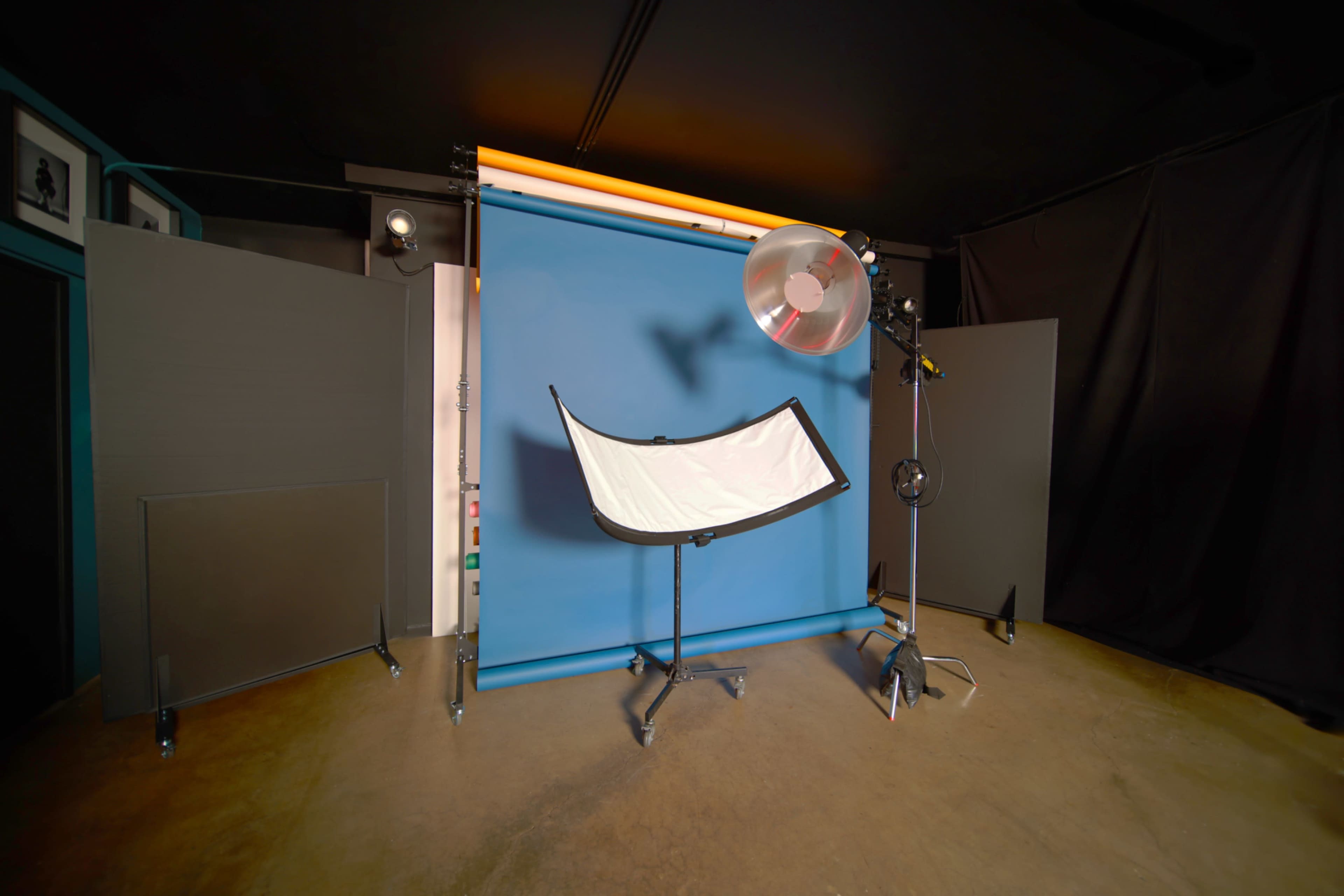 The image shows a photography setup with a blue backdrop, a reflector, and lighting equipment in a studio environment.