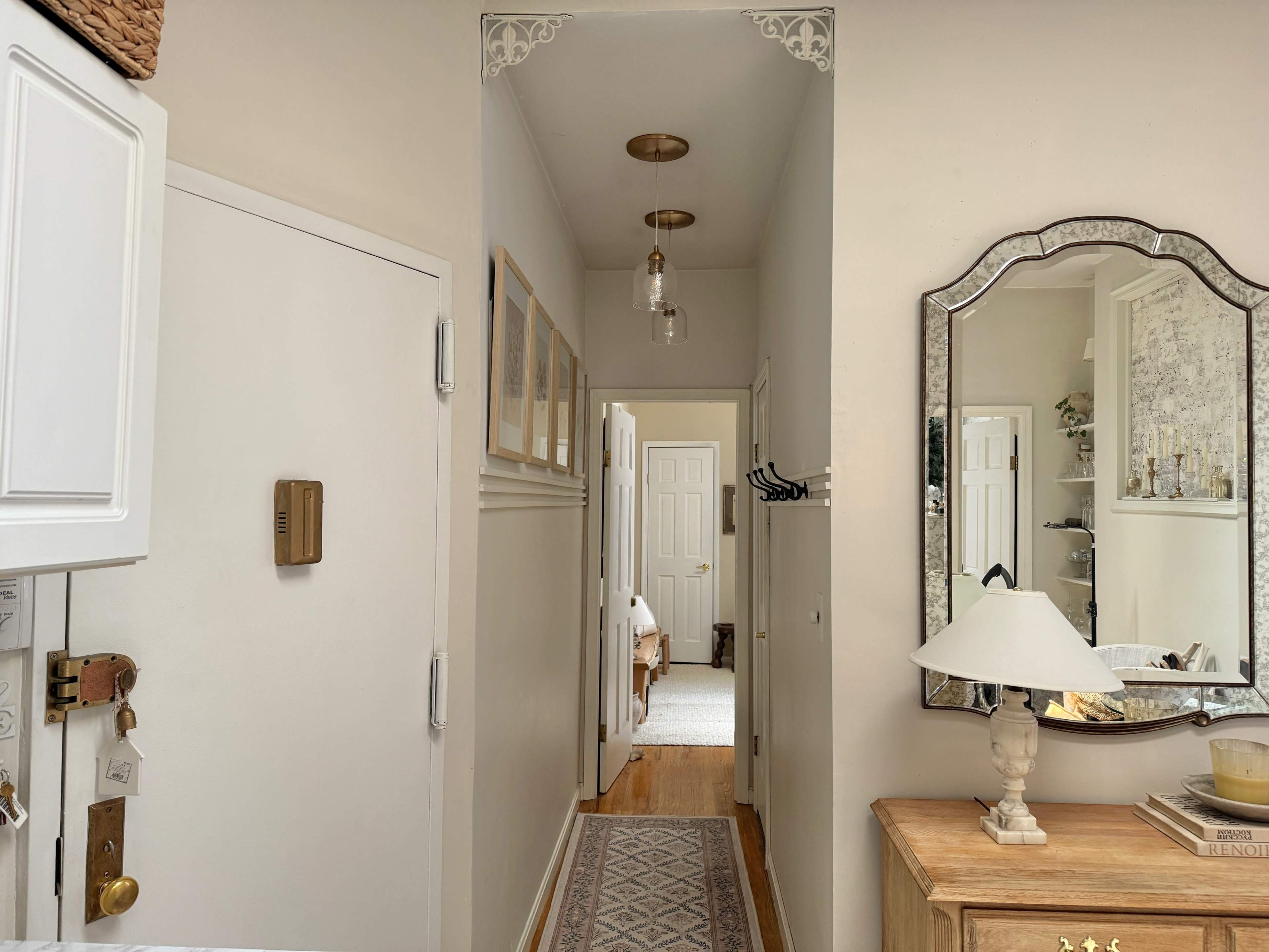 A narrow hallway with doors on both sides, featuring a mirror and a lamp on a wooden console table.
