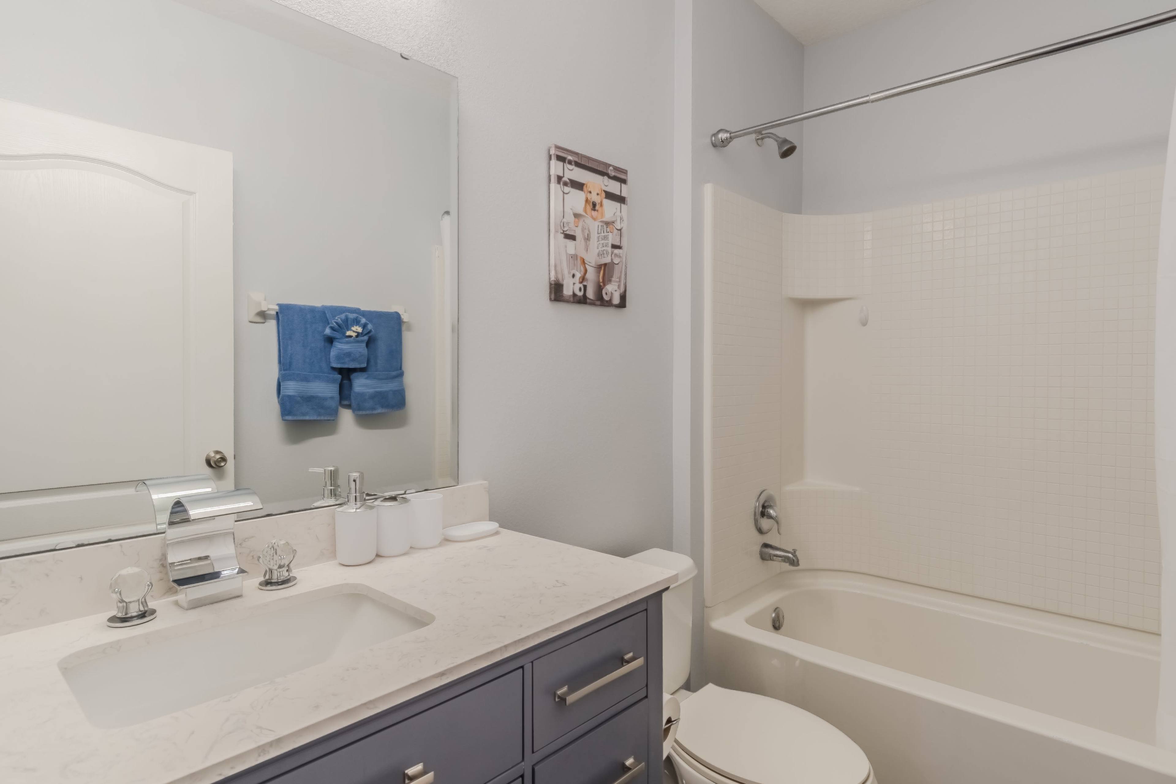 A bathroom with a white bathtub, a blue towel hanging, and a counter with a sink and toiletries.
