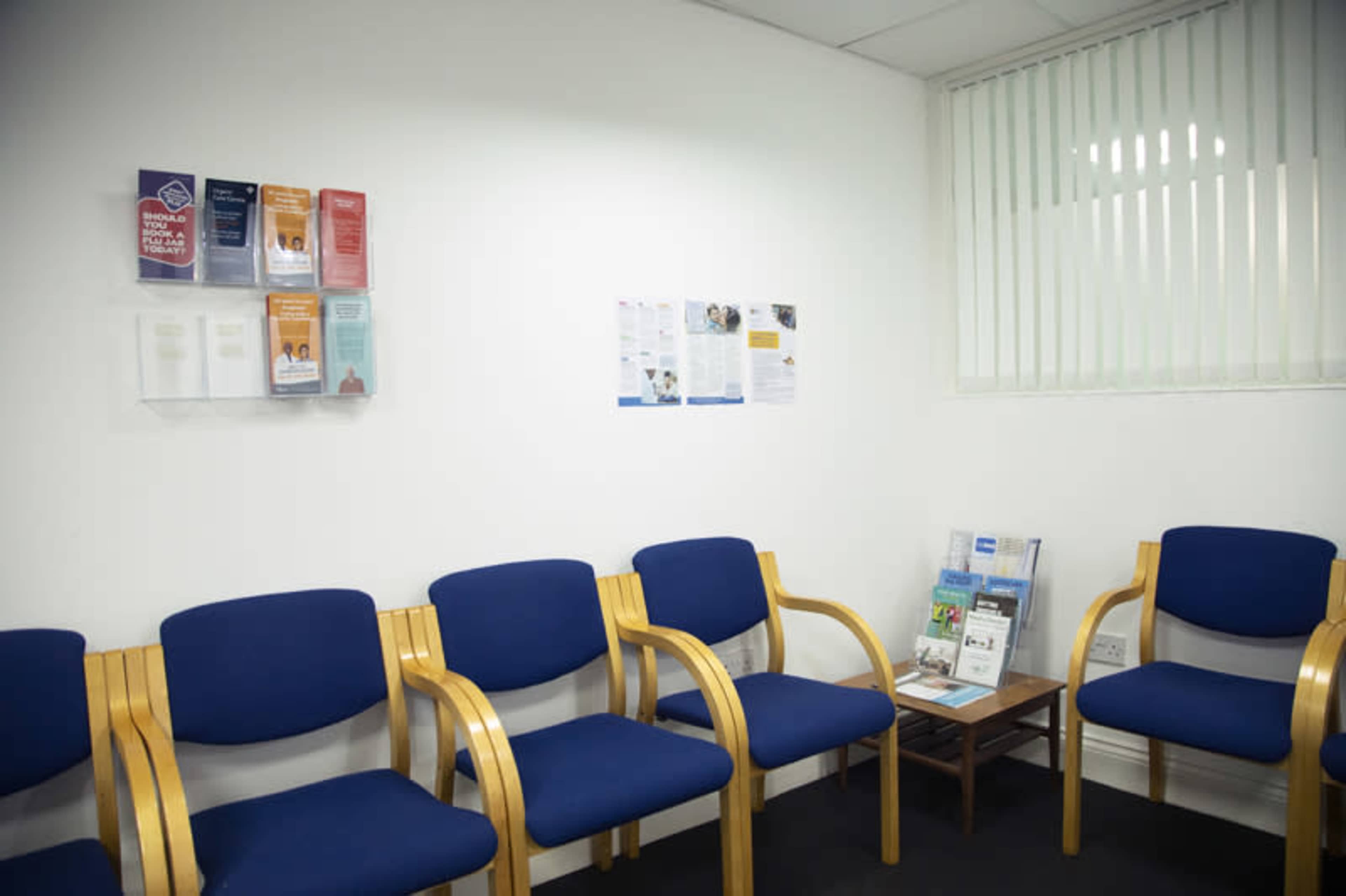A waiting room with blue chairs arranged against a white wall, featuring informational brochures displayed in holders.