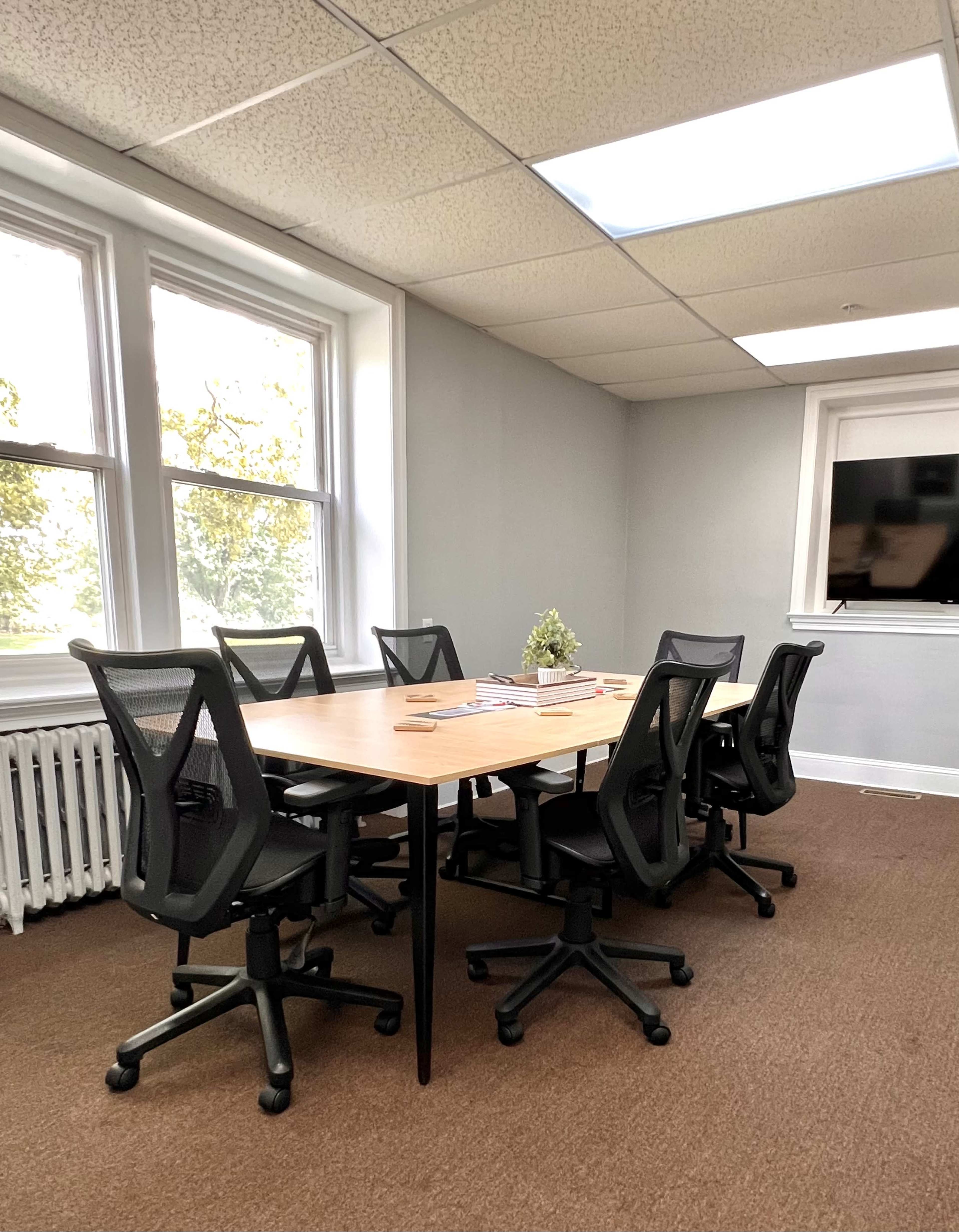 A well-lit conference room features a large table surrounded by ergonomic chairs and a window with natural light.