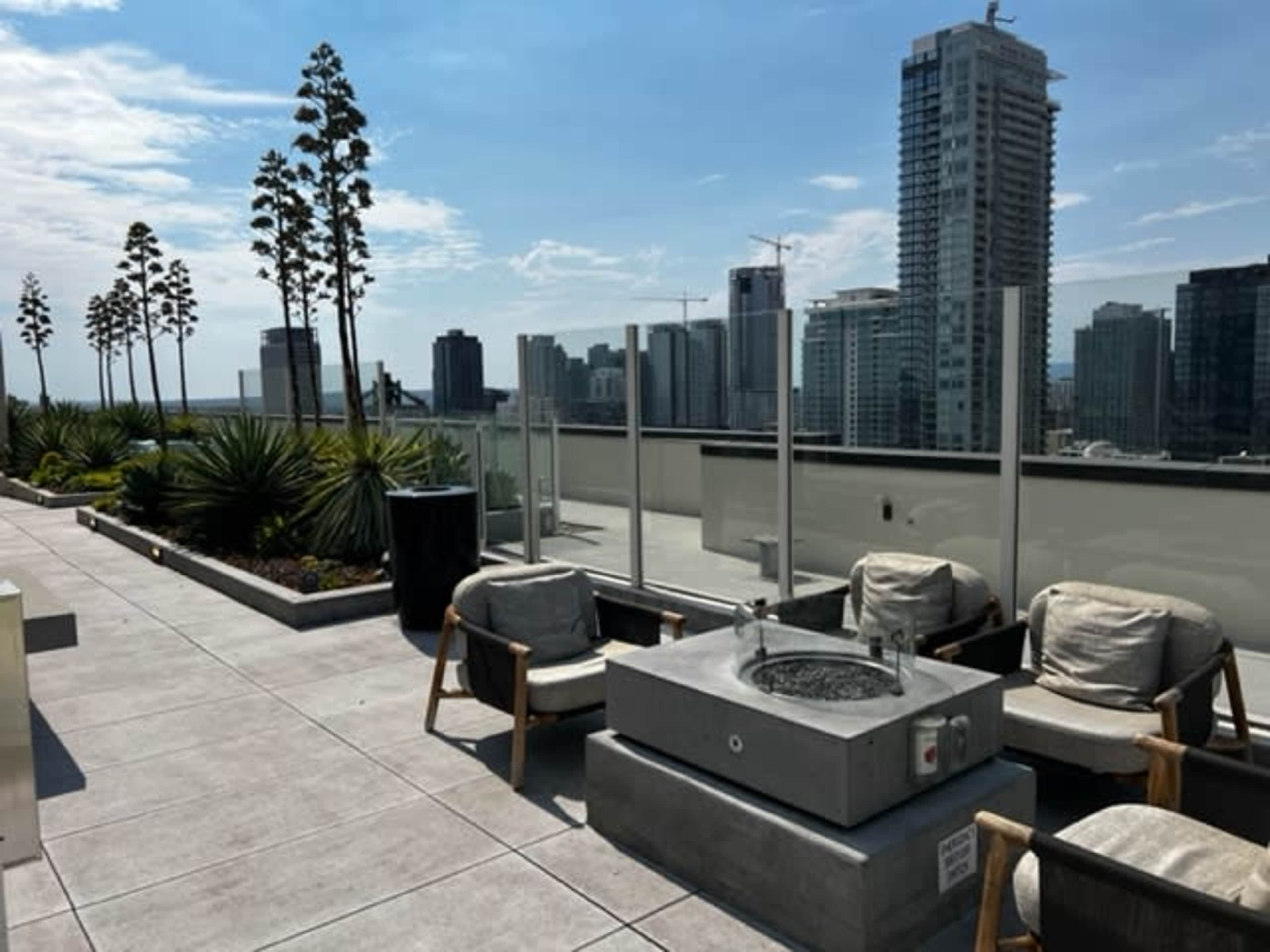 A rooftop terrace with seating, planters, and a view of city skyscrapers.