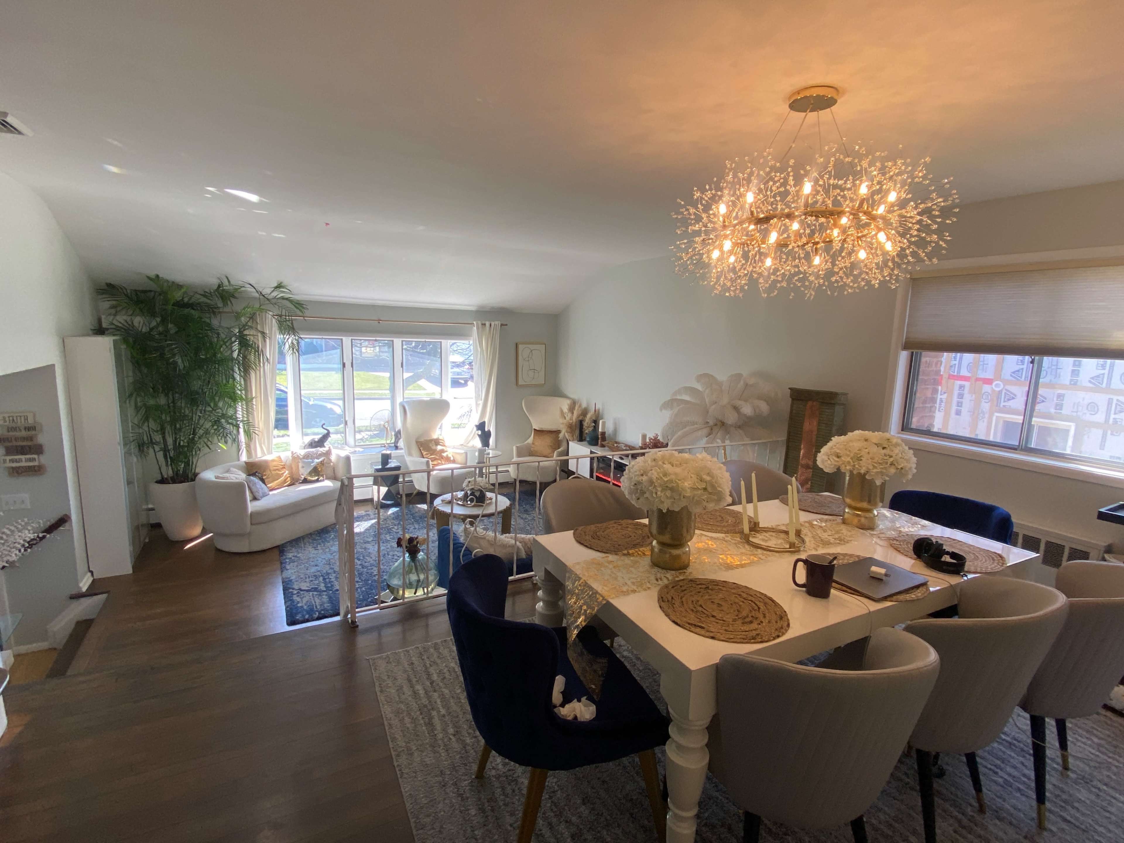A modern dining area with a table surrounded by upholstered chairs, complemented by a bright living space filled with plants and natural light.