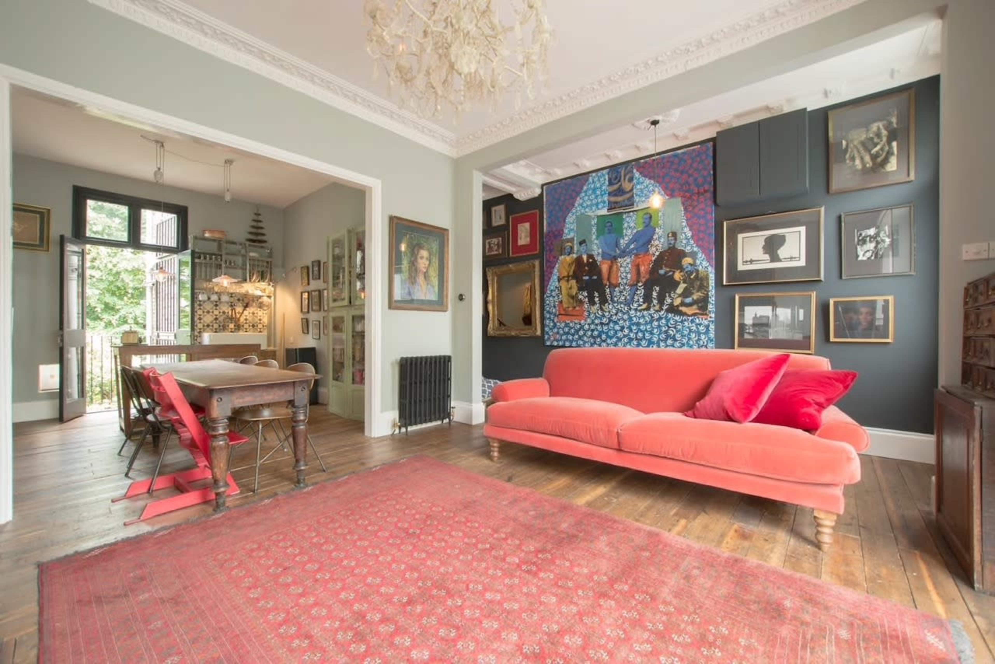 A spacious living area featuring a red velvet sofa, an intricately patterned rug, and a gallery wall with various framed artworks.