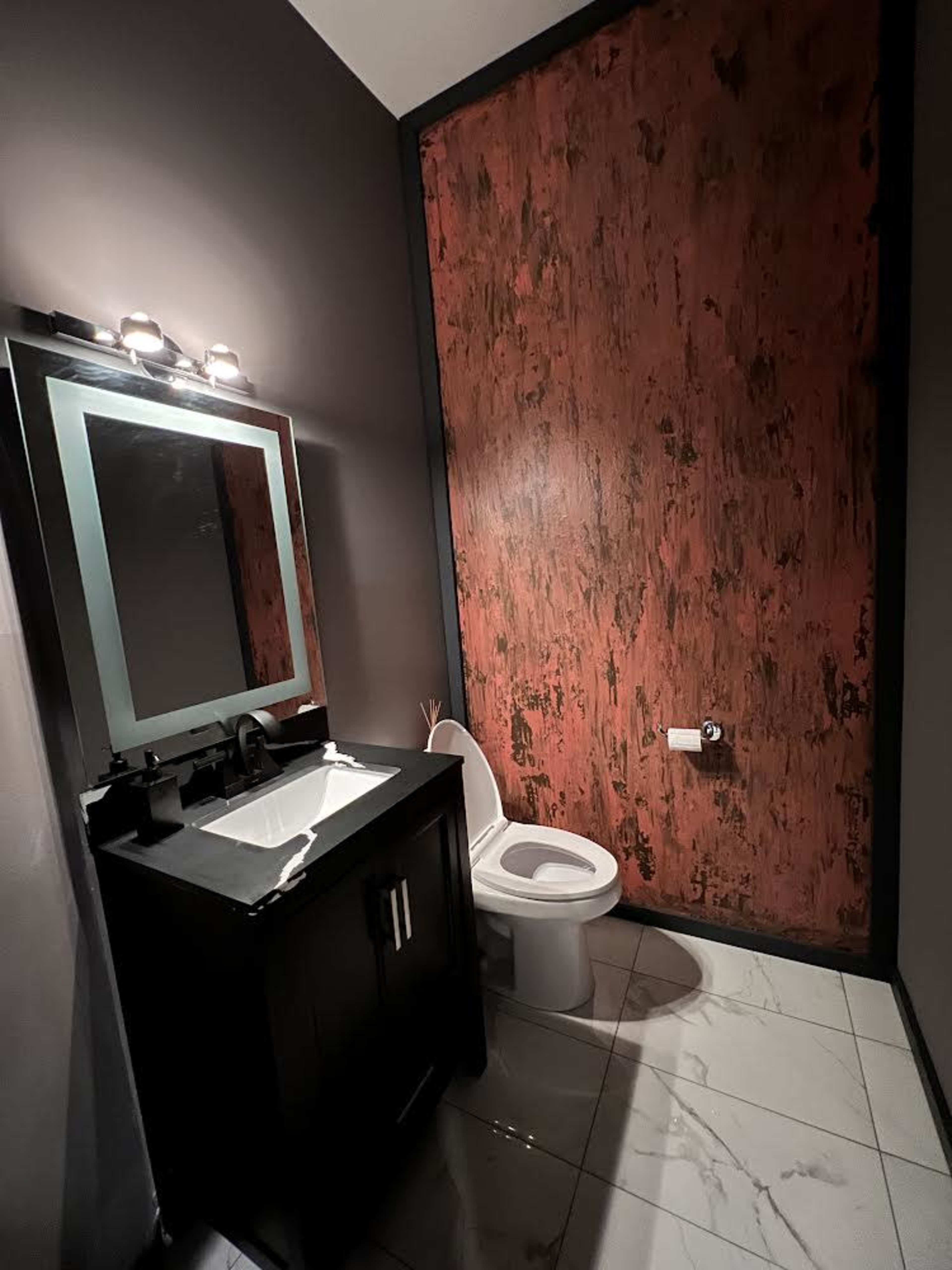 A small bathroom featuring a black vanity with a sink, a modern mirror, a white toilet, and a marbled floor.