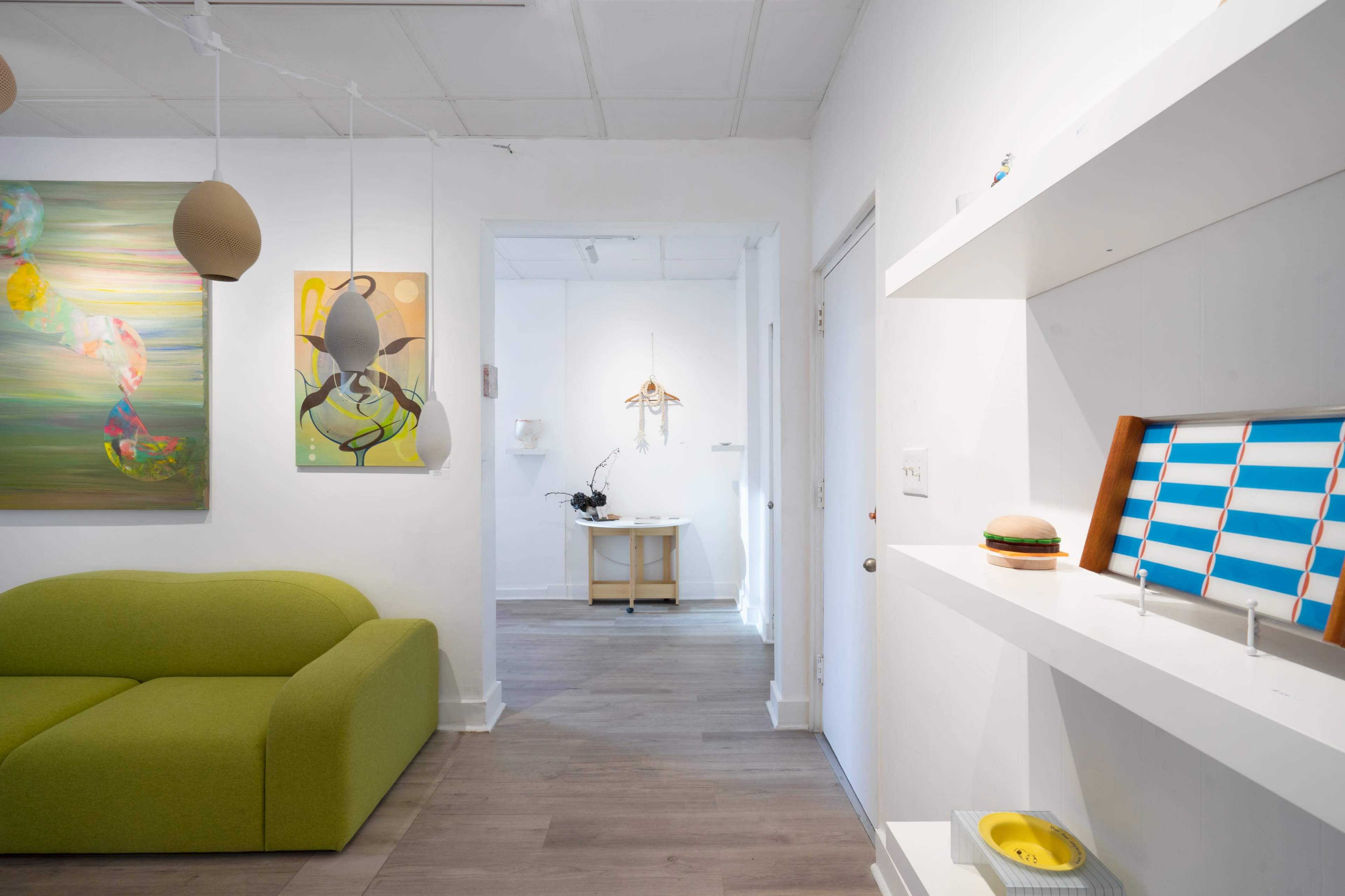 The image shows a bright, modern interior with green furniture, wall art, and a hallway leading to another room.