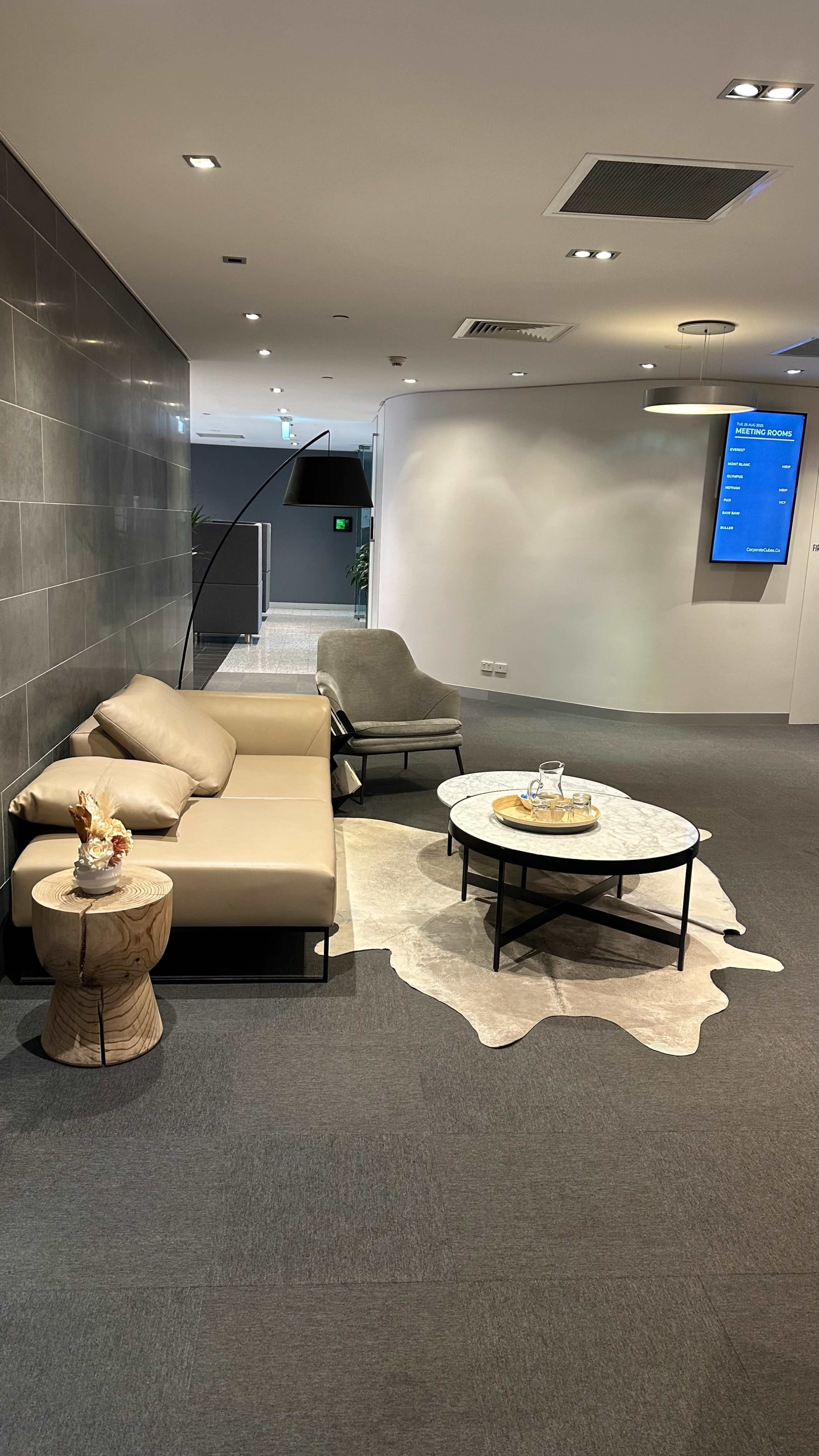 The image shows a modern lounge area featuring a light-colored sofa, a round marble coffee table, a wooden stool, and a cowhide rug on the floor.