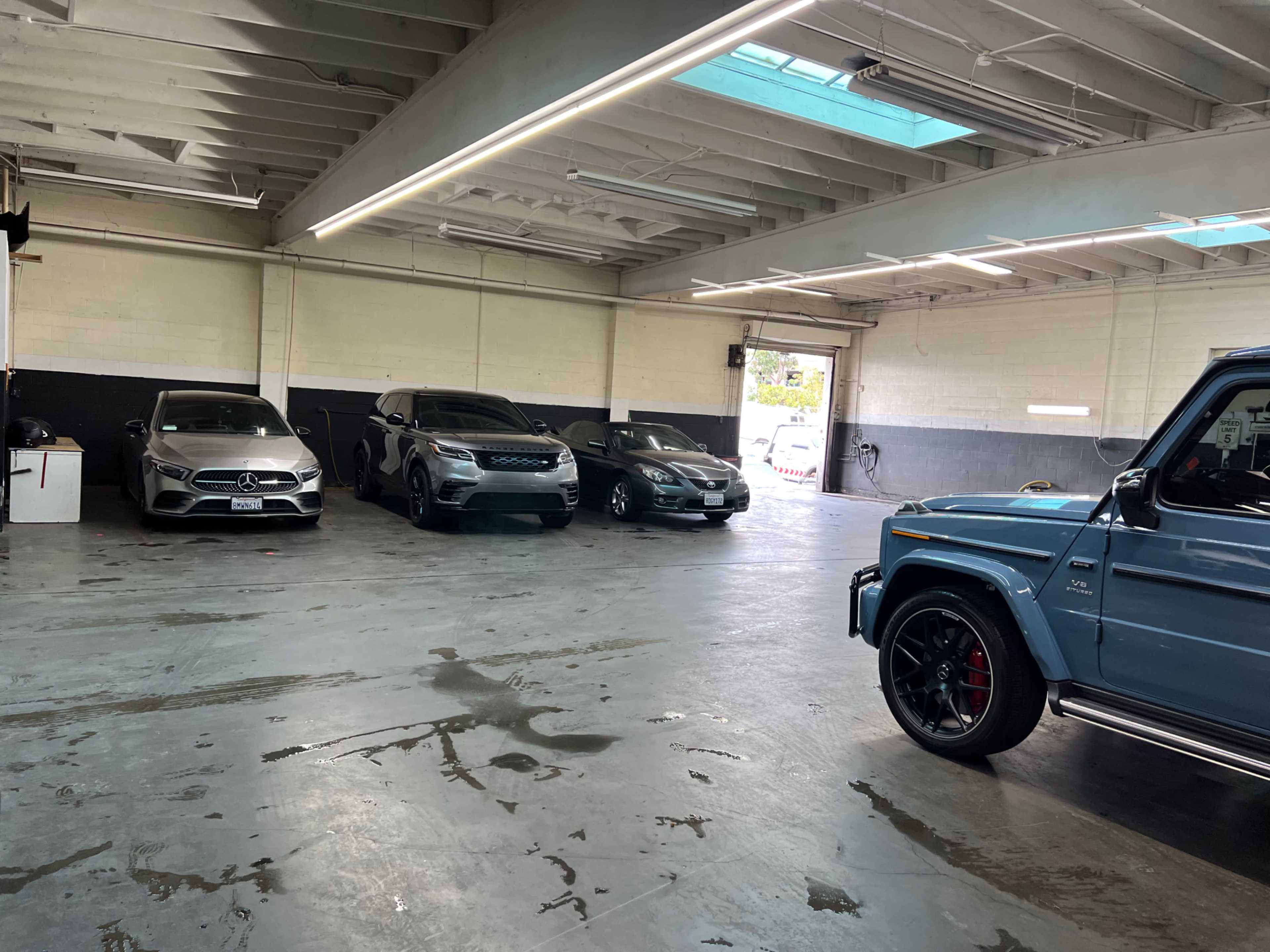 The image shows a spacious garage with four cars parked, including a blue SUV and three sedans, under a well-lit ceiling.