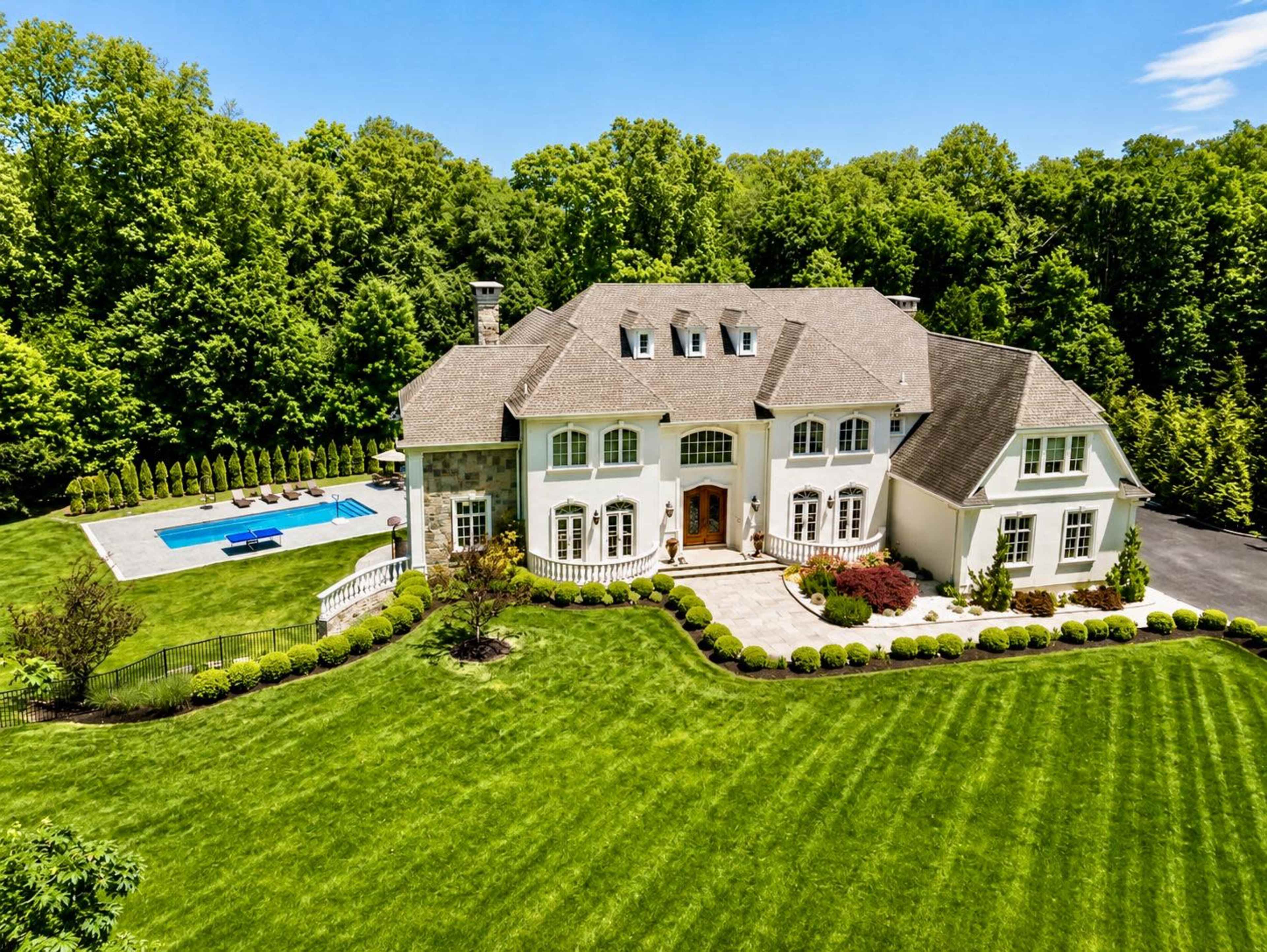 The image shows a large, two-story house with a manicured lawn and a swimming pool in the backyard, surrounded by trees.