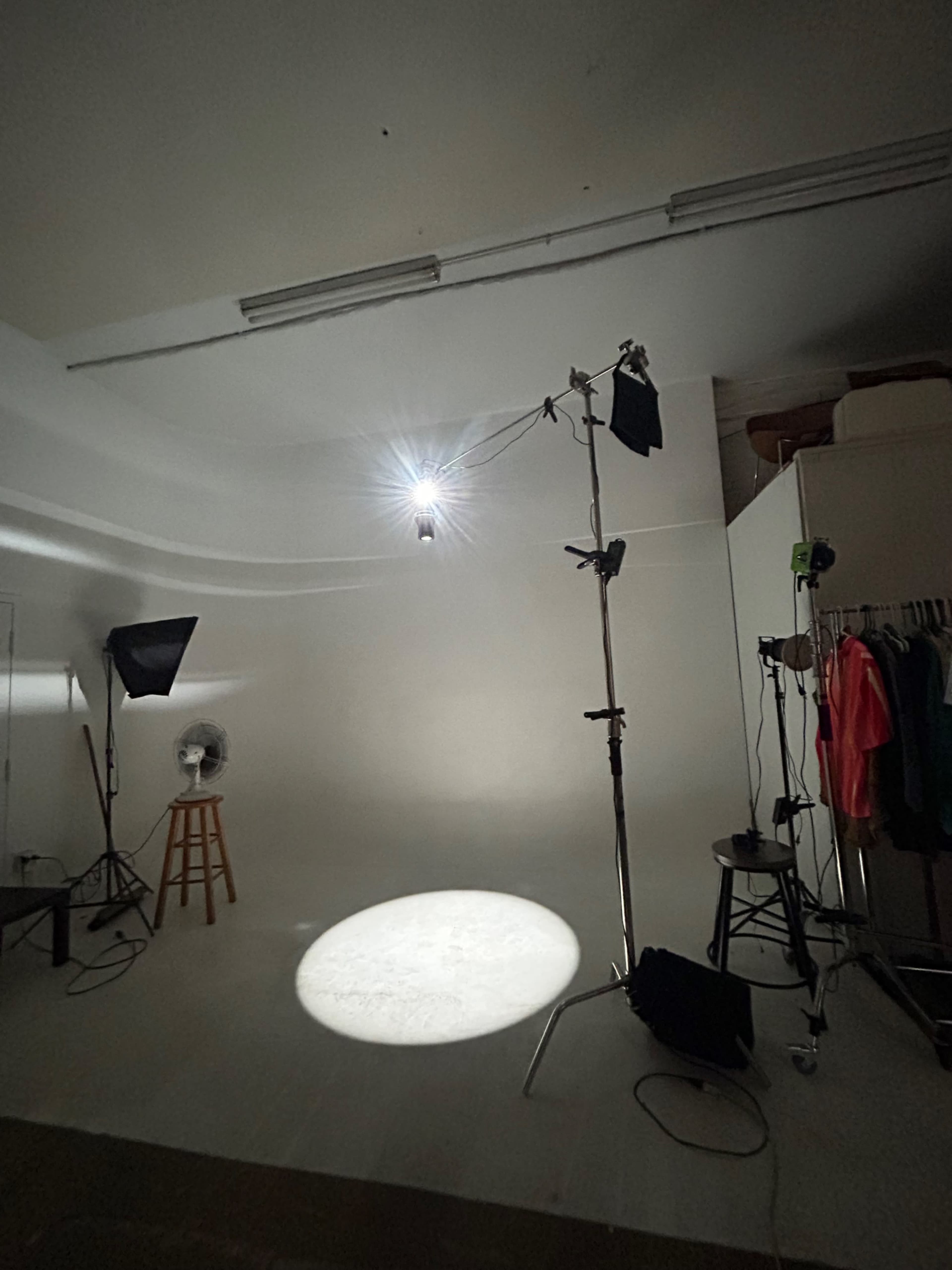 A photography studio is set up with multiple lighting fixtures and a fan, featuring a spot of light on the floor against a plain background.