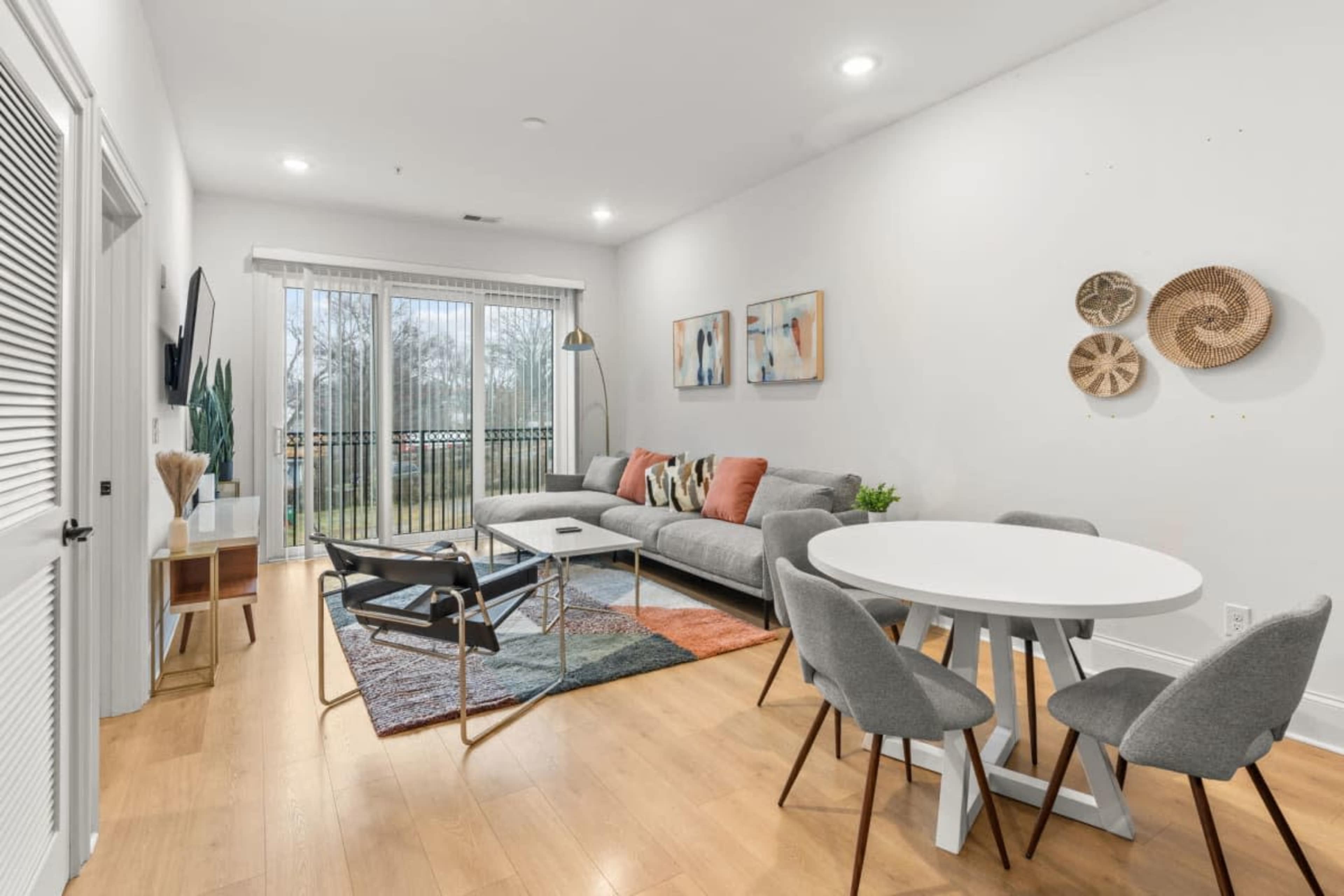 A modern living room features a gray sofa, a round dining table with chairs, and large sliding glass doors leading to a patio.
