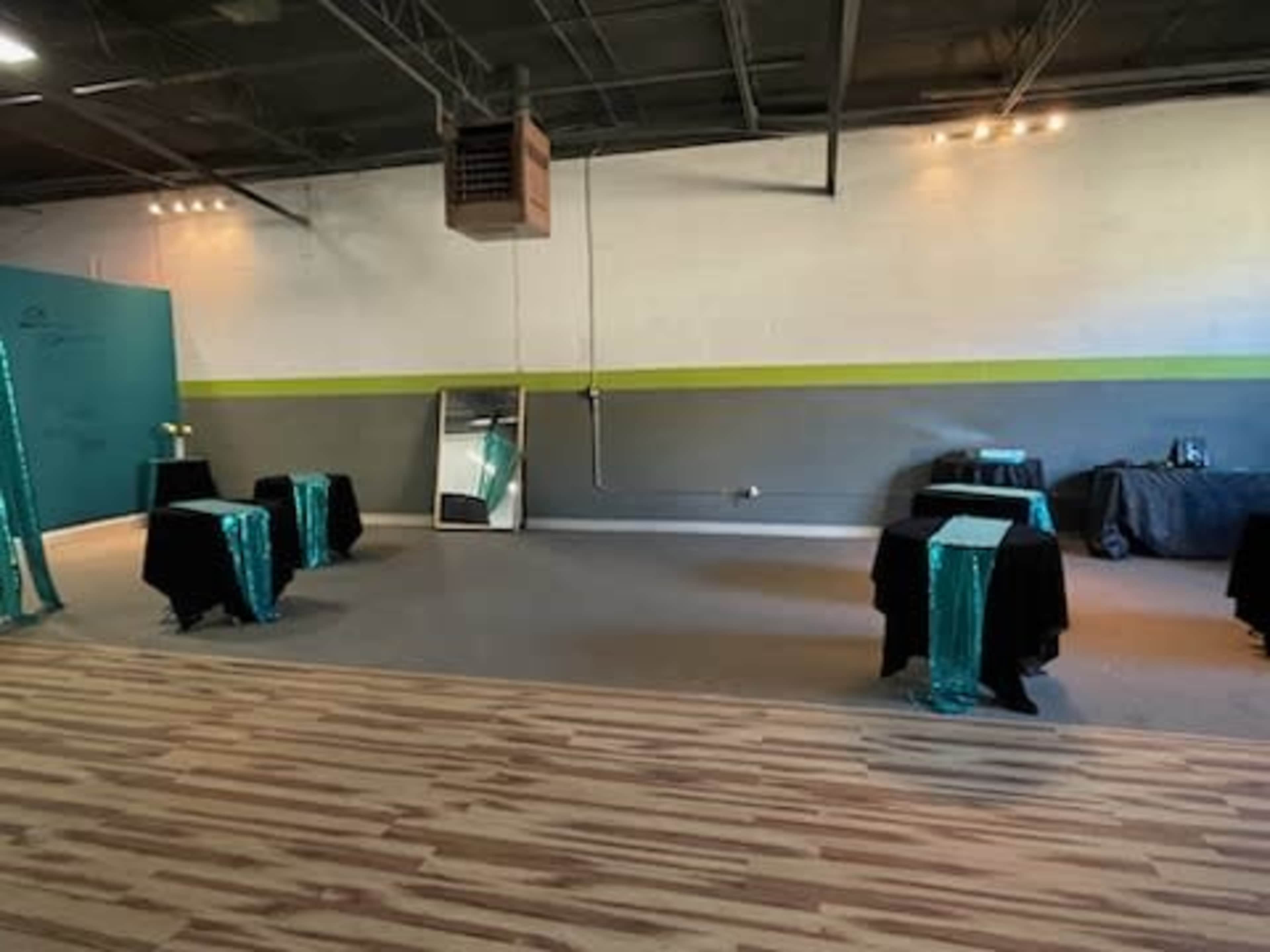 A spacious event room with several black tables covered in teal tablecloths and a large mirror leaning against a wall.