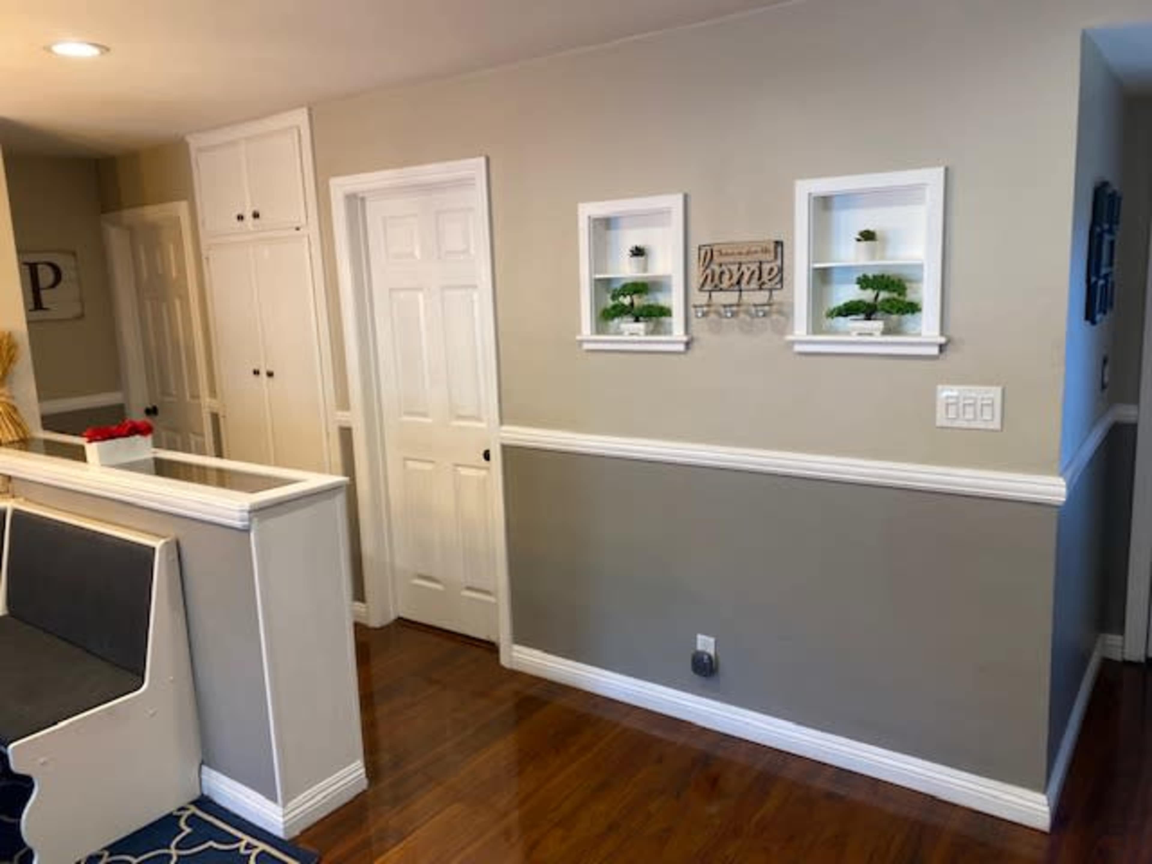 A hallway with a wooden floor, white wainscoting, and a couple of small wall-mounted shelves containing plants.