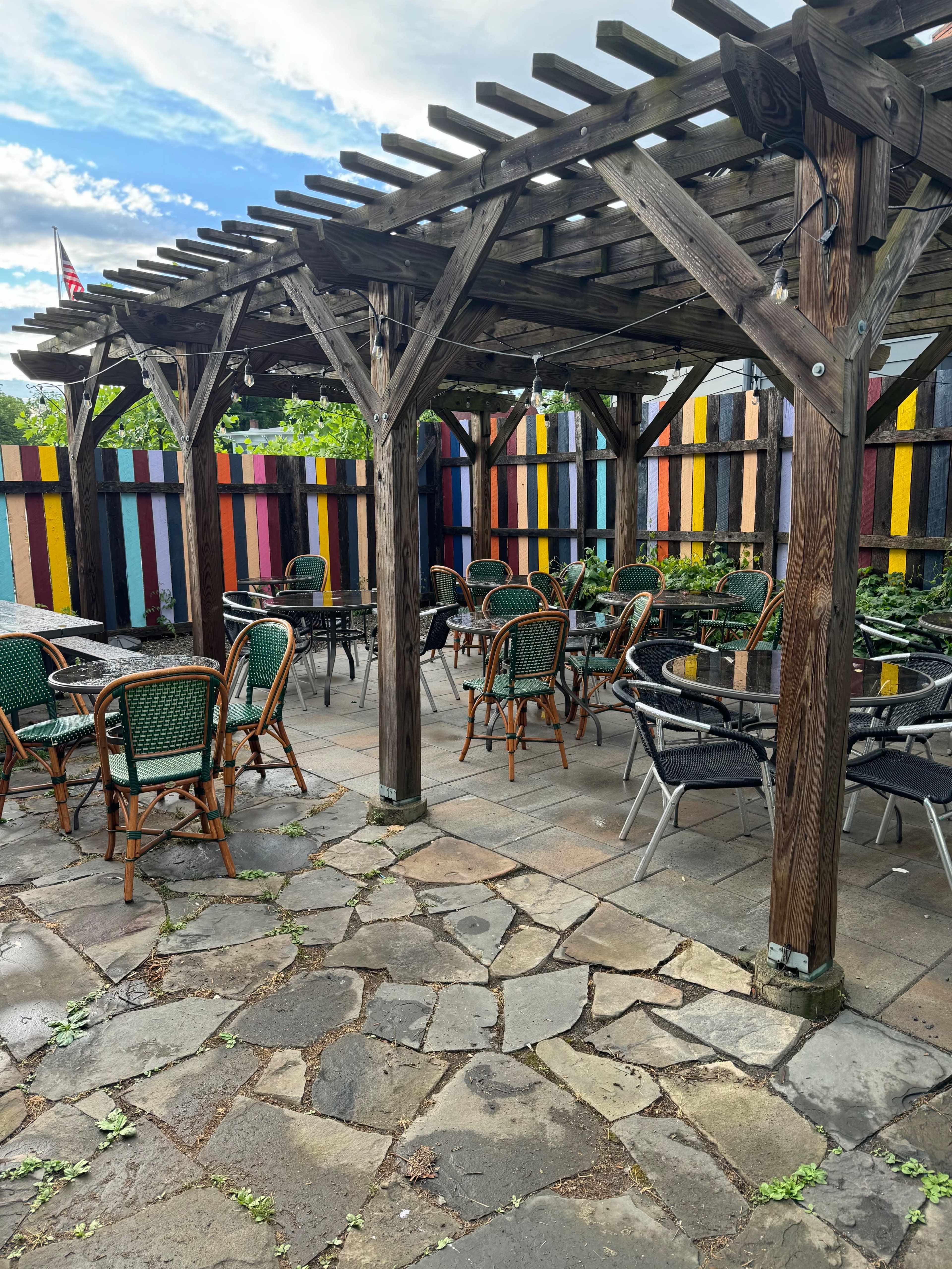 A patio area features wooden pergolas, stone flooring, and patio furniture surrounded by colorful wooden walls.
