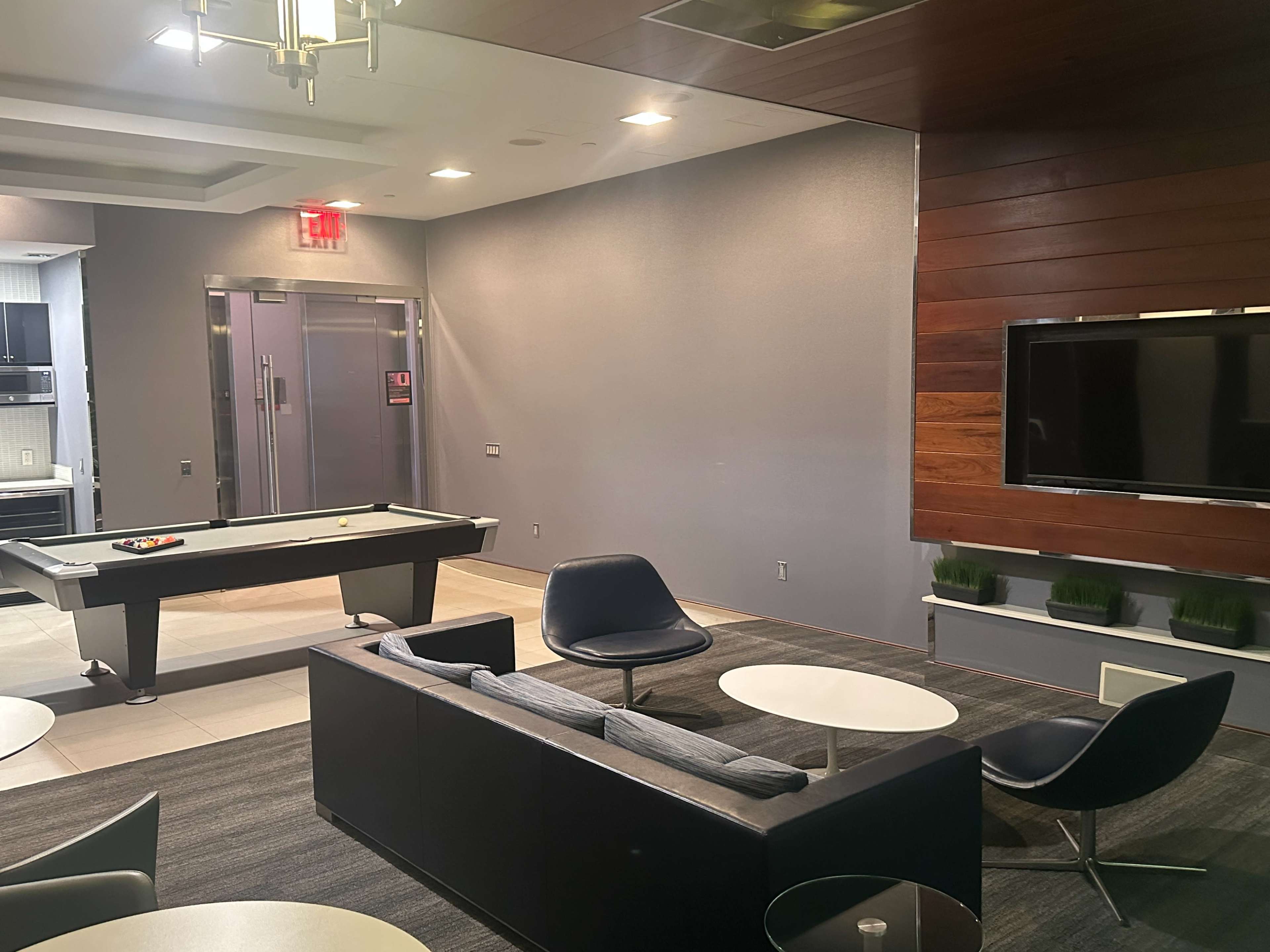 The image shows a modern lounge area featuring a pool table, several lounge chairs, and a wall-mounted TV.