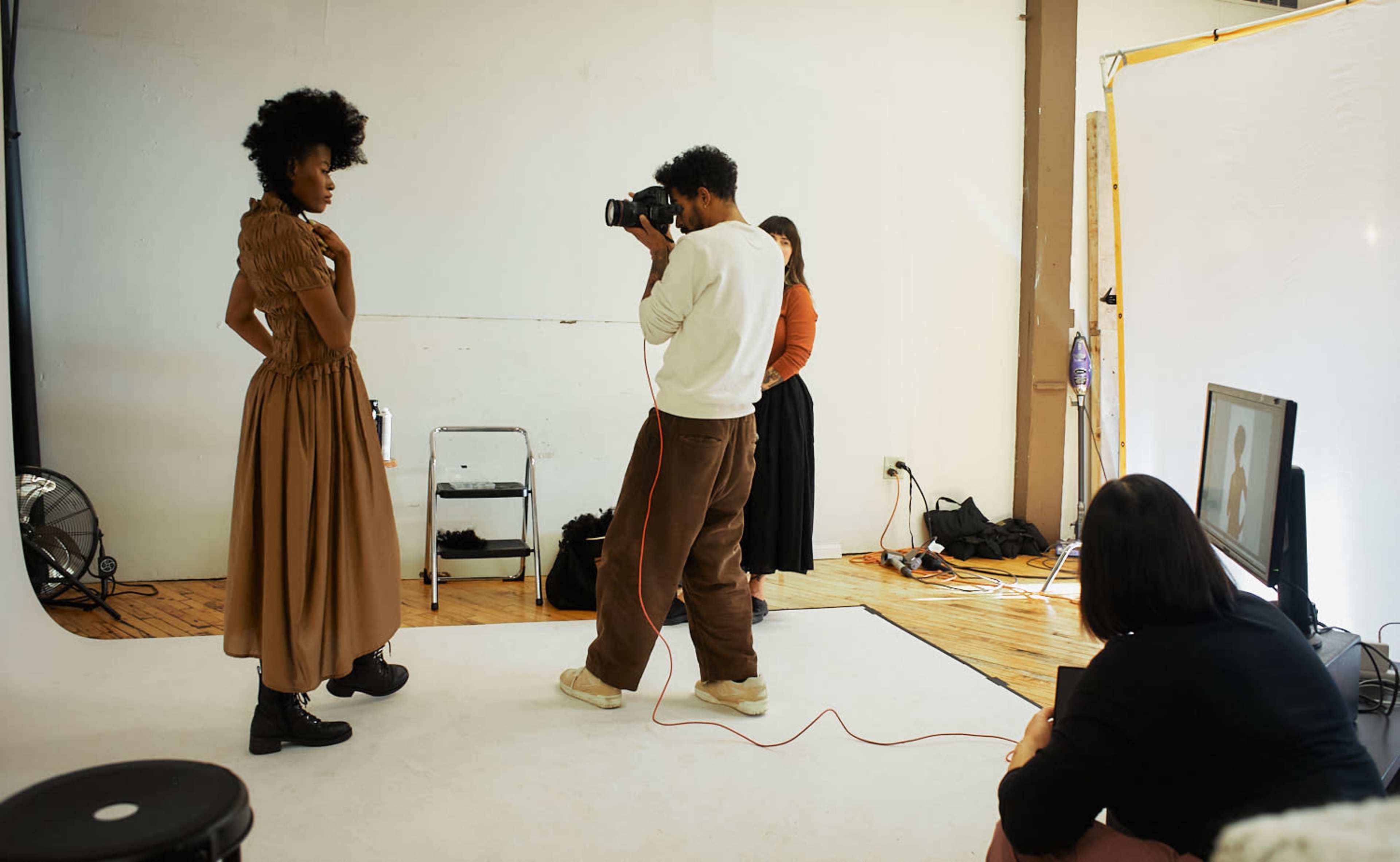 A photographer captures an image of a model wearing a long dress in a studio setting while two people observe.