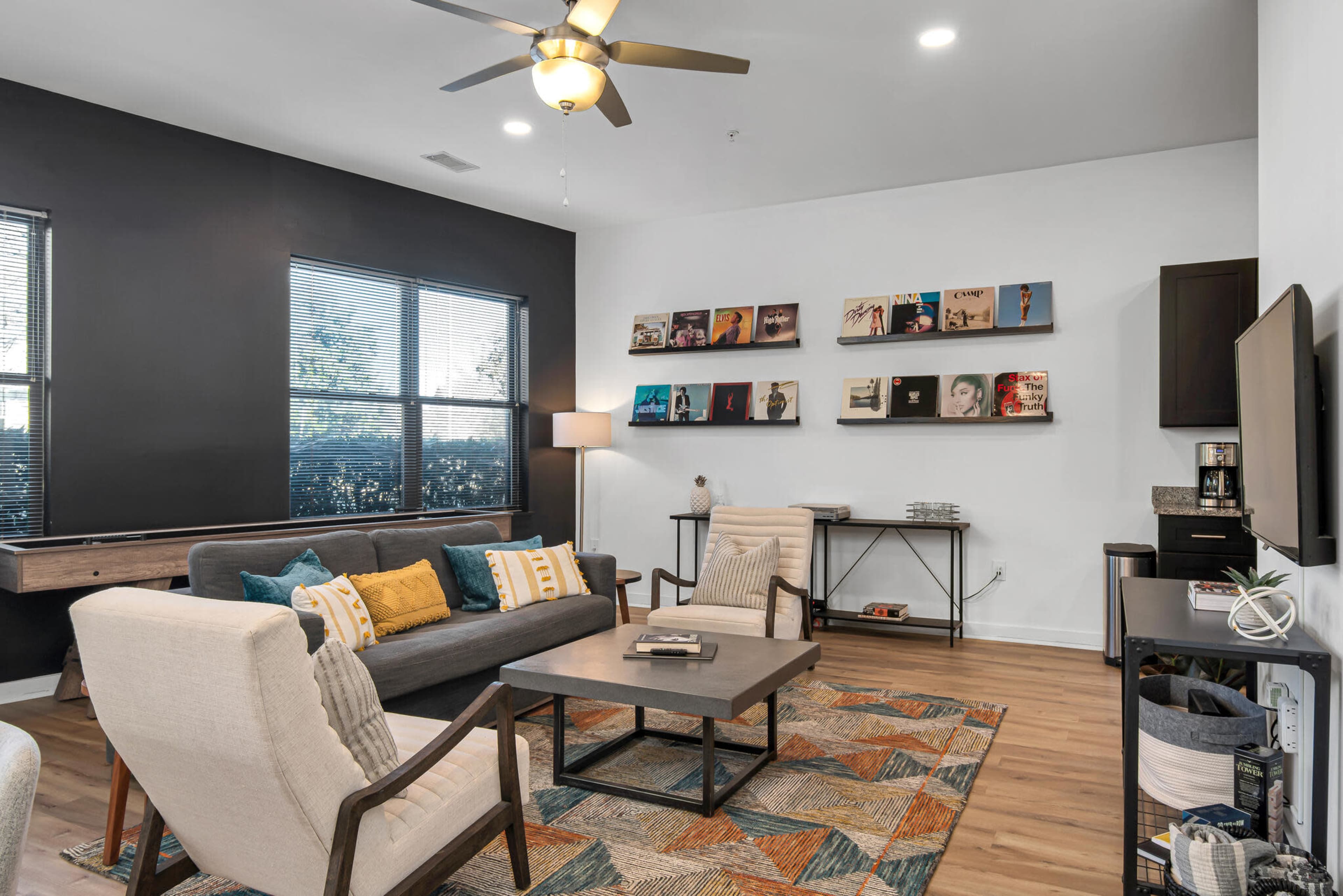 The image shows a modern living room with a gray sofa, two chairs, a coffee table, and a wall displaying framed artwork.