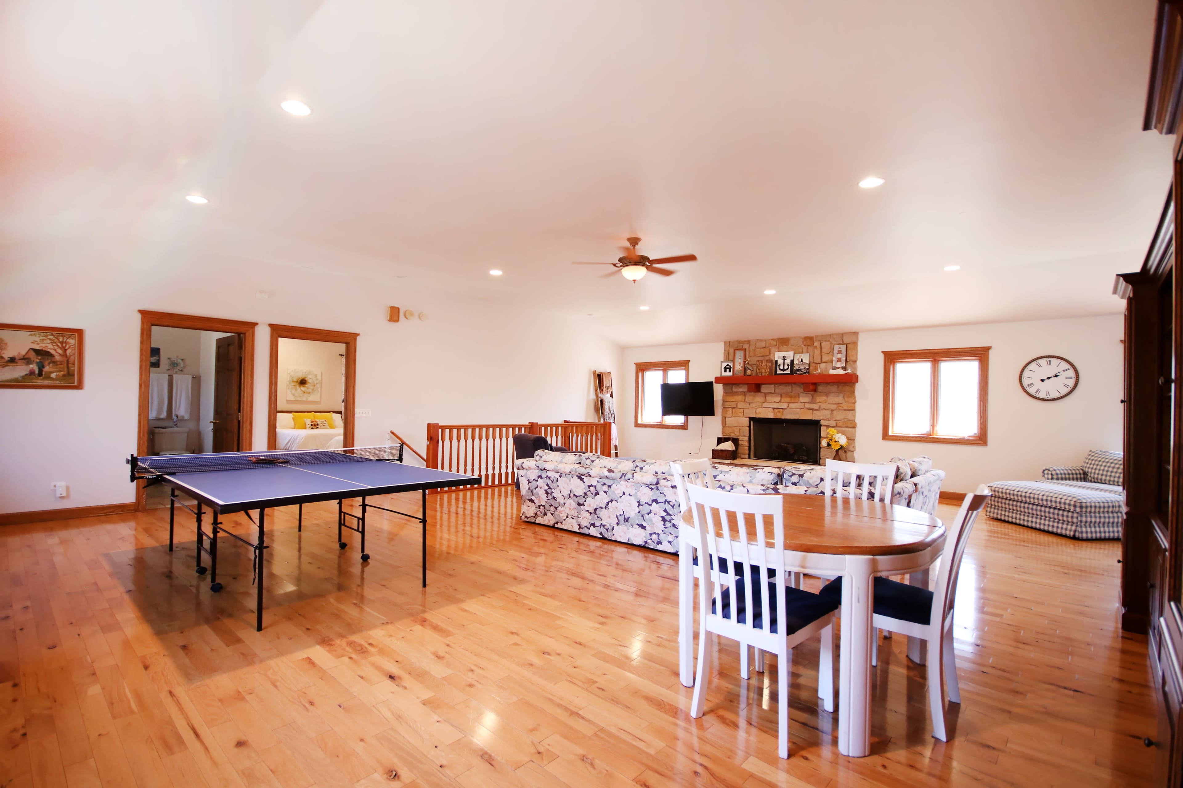 A spacious living area featuring a ping pong table, a dining table with chairs, a sofa, and a stone fireplace.