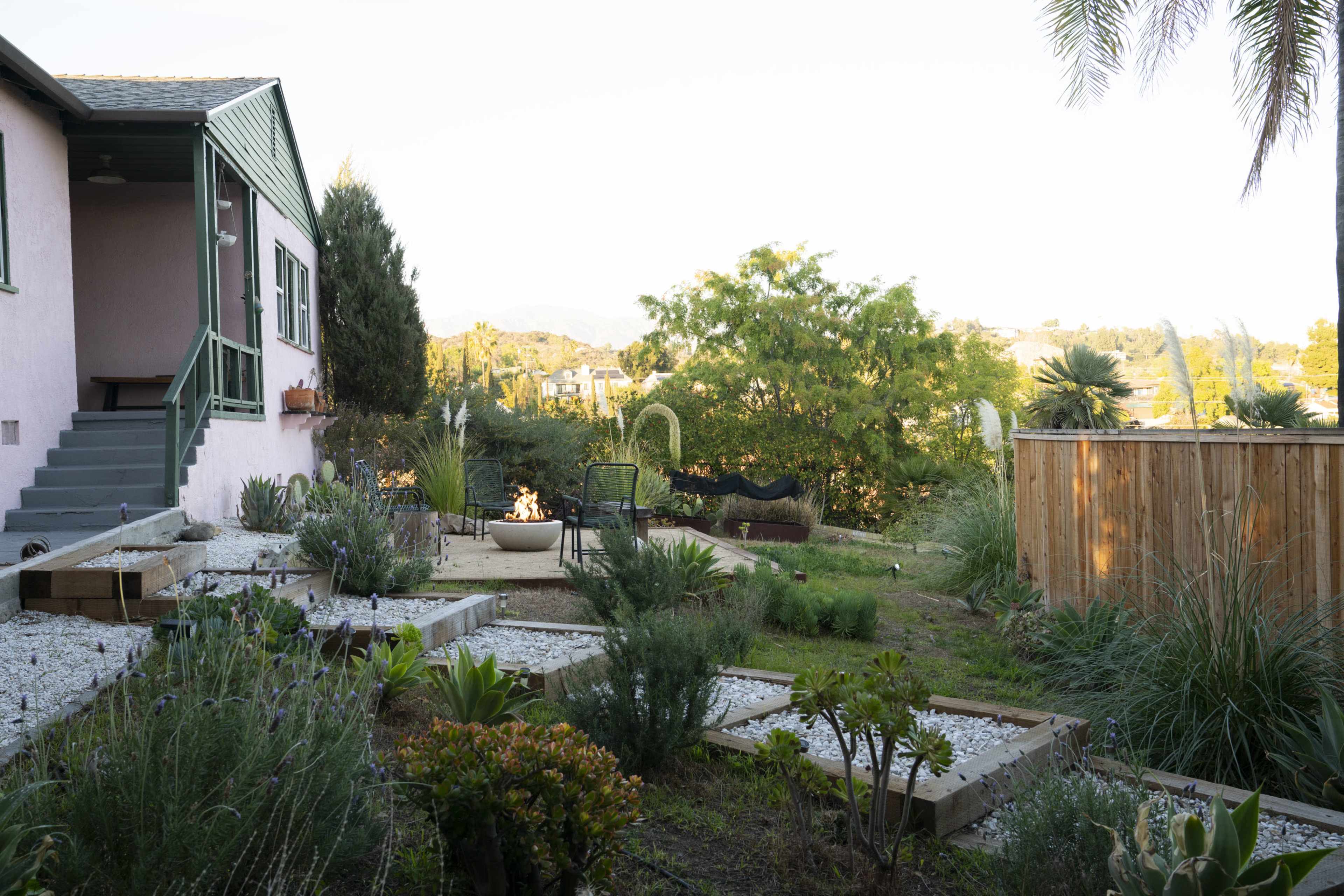 A backyard garden features raised plant beds, a hammock, and a view of surrounding greenery and hills.