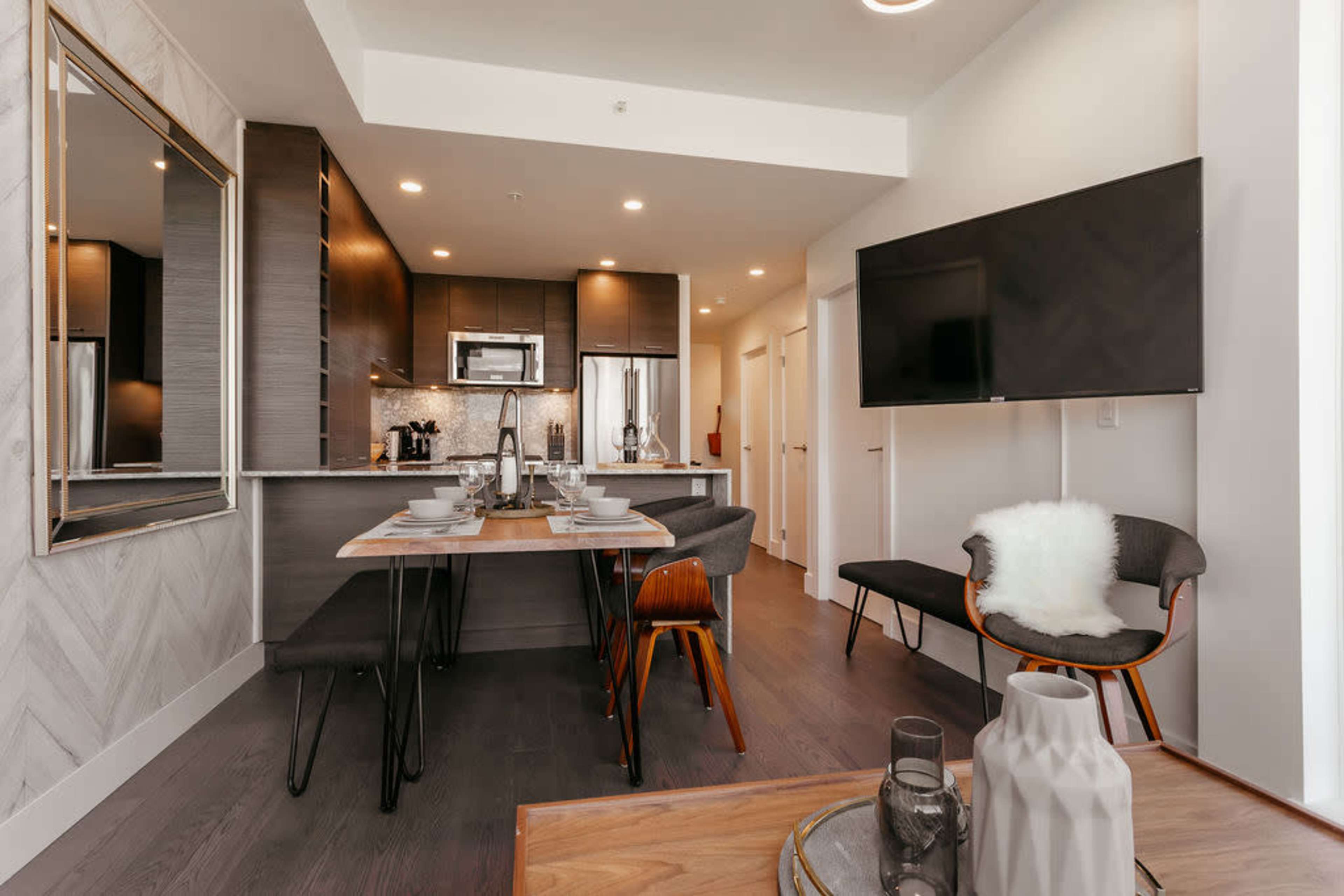 A modern kitchen and dining area with a table set for a meal, sleek cabinetry, and contemporary furnishings.