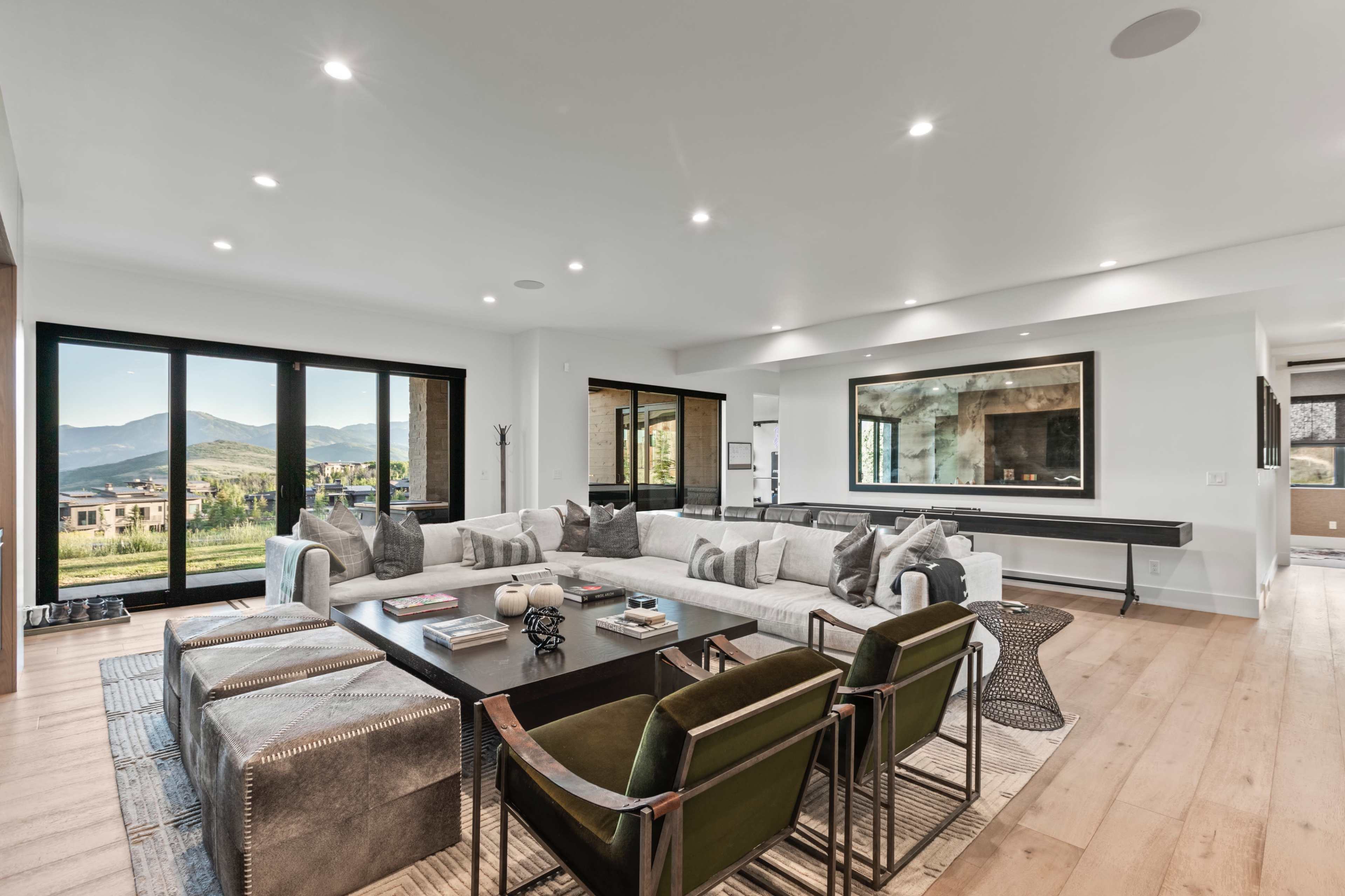 The living room features a large sectional sofa and two green chairs, with a coffee table at the center and large windows showcasing a mountain view.